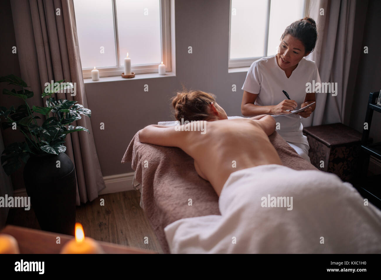 Weibliche Massage therapist Gespräch mit Frau im Wellnesscenter und Notizen zu machen. Kosmetikerin Prüfung der weiblichen Kunden vor der Kur. Stockfoto