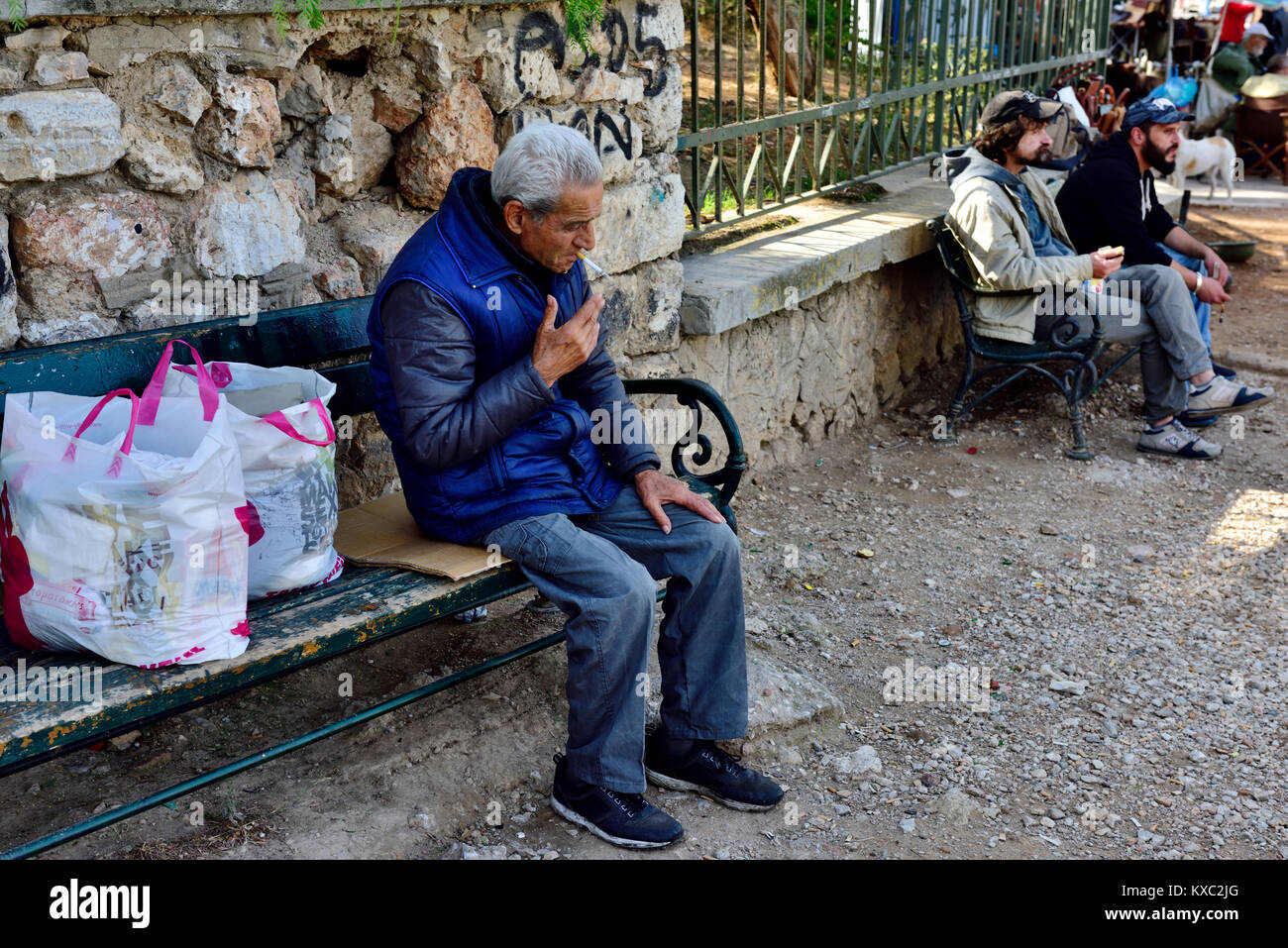 Älteren griechischen Mann entspannend, draußen sitzt auf der Bank mit Tüten, Athen, Griechenland Stockfoto
