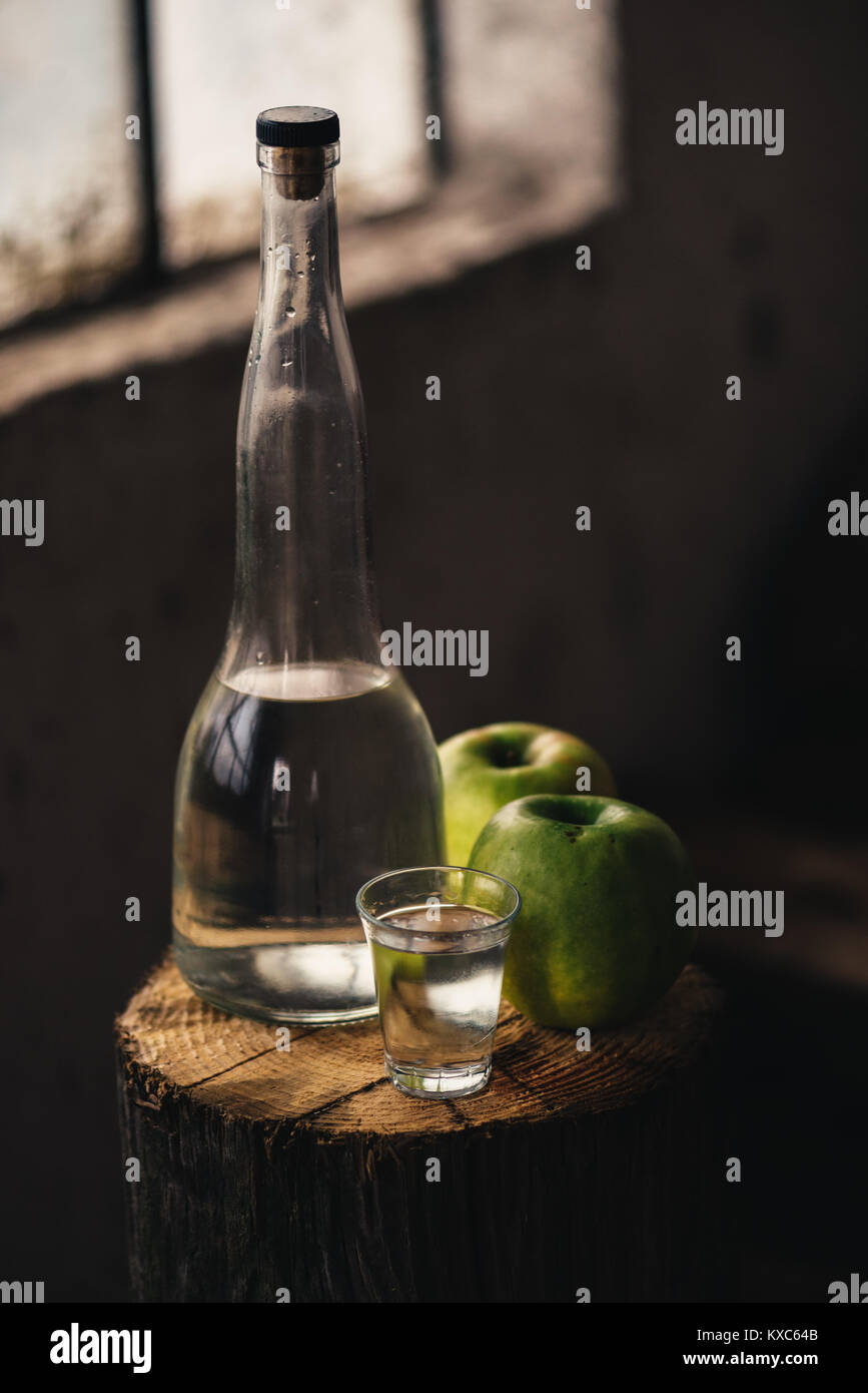 Apple Brandy, rustikale Atmosphäre. Flasche und single shot Glas mit Alkohol trinken und zwei grüne Apfel Obst. Stockfoto