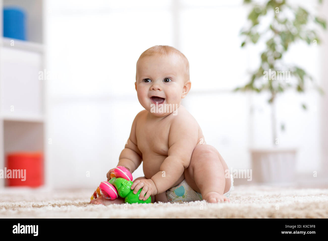 Cute Baby in Windel sitzt auf dem Teppich und spielt mit Spielzeug zu Hause. Geringe Tiefenschärfe. Stockfoto