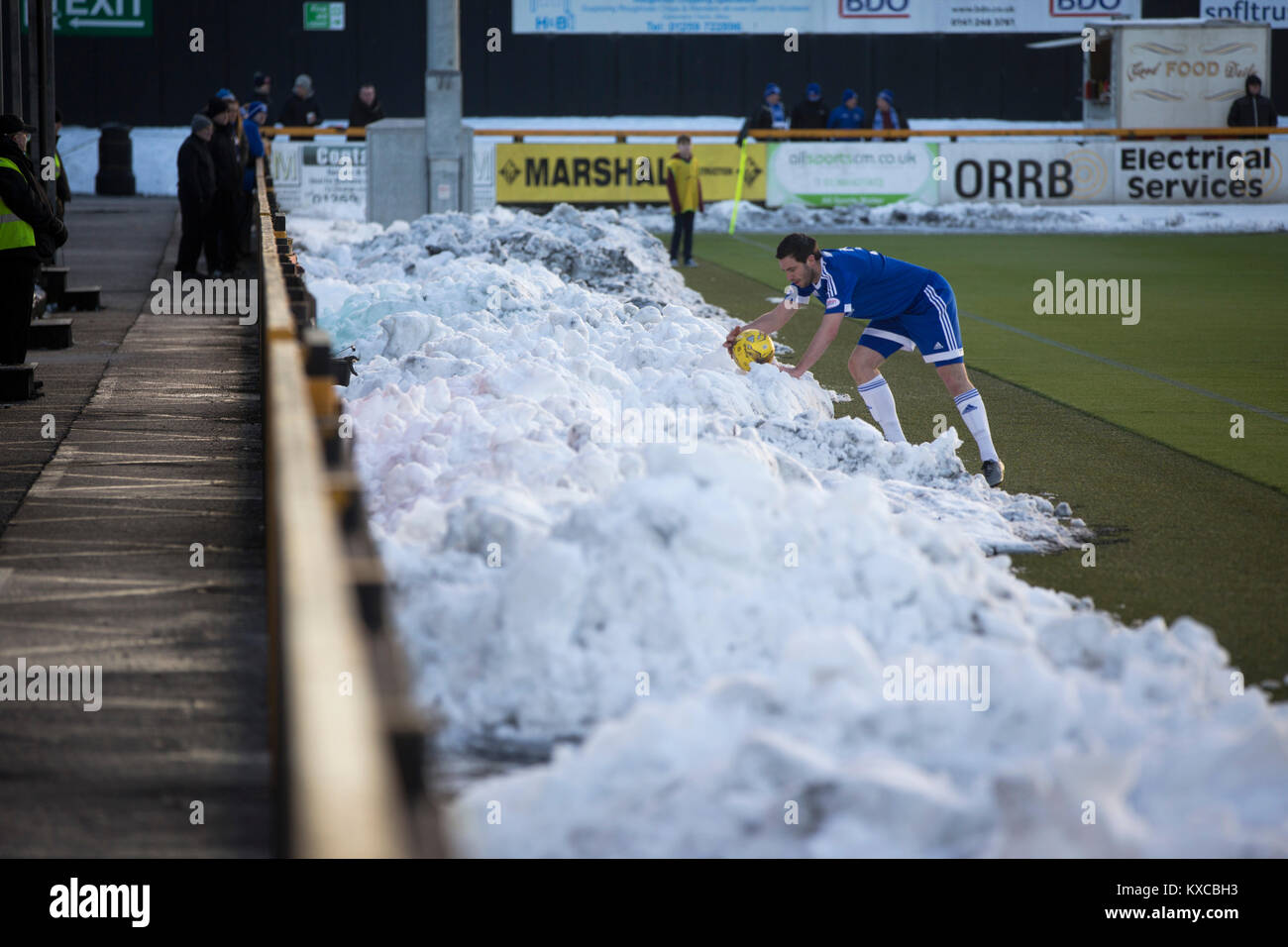 Ein away Player ruft den matchball von einem Haufen Schnee als Alloa Athletic in Peterhead (in Blau) in einem schottischen Liga eine Befestigung am Freizeitpark, mit den Ochil Hills im Hintergrund. Der Verein wurde 1878 als clackmannan County gebildet, die Namen ändern und die alloa Athletic 1883. Die Besucher gewann das Spiel durch ein Ziel zu Null, von einer Menge von 504 beobachtet. Stockfoto