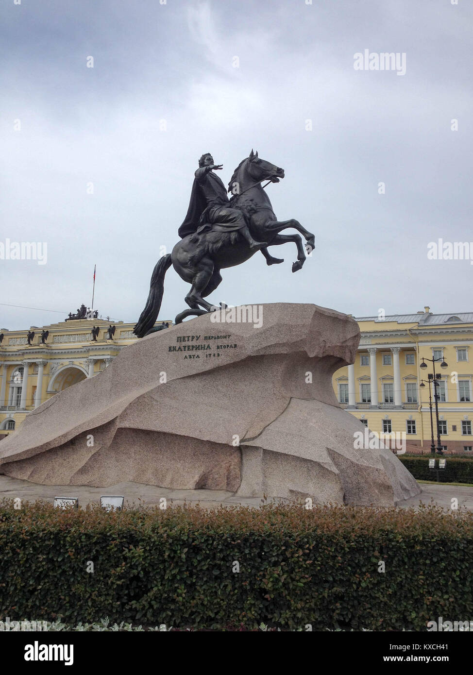Der Bronzene Reiter - Seitenansicht der Statue von Peter dem Großen mit einem gelben Gebäude im Hintergrund, an einem bewölkten Tag, in St. Petersburg, Russland Stockfoto