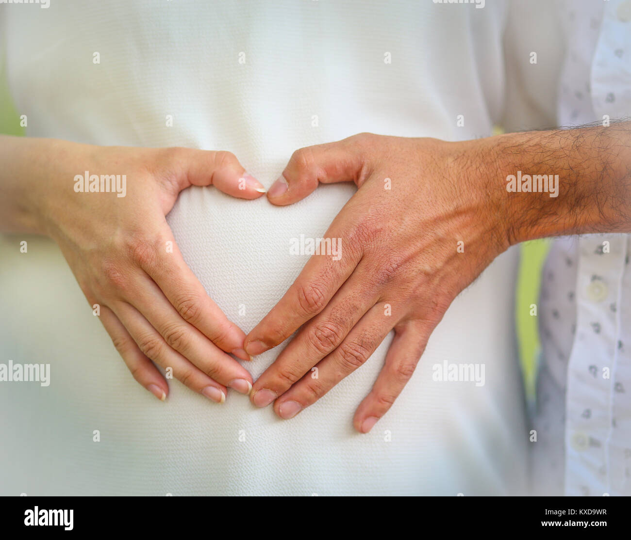 In Herzform die Hände über dem Bauch der Schwangerschaft - in die Hände eines Mannes und einer Frau zusammen in Form eines Herzens trat über dem Bauch einer schwangeren Frau Stockfoto