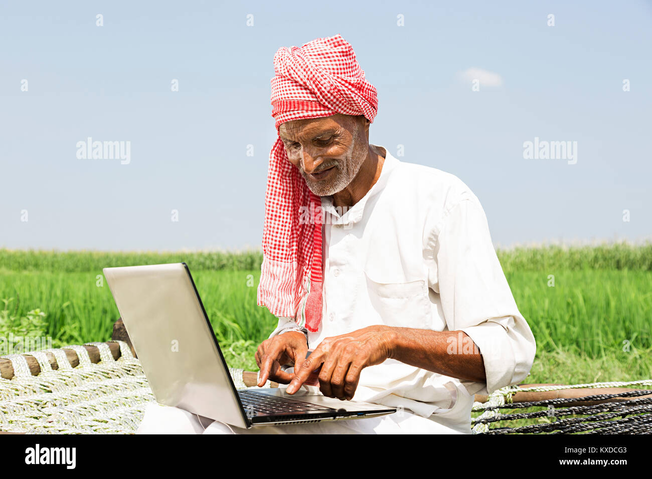 1 indischen Bauern älterer Mann sitzt Kinderbett Bauernhof mit Laptop Stockfoto