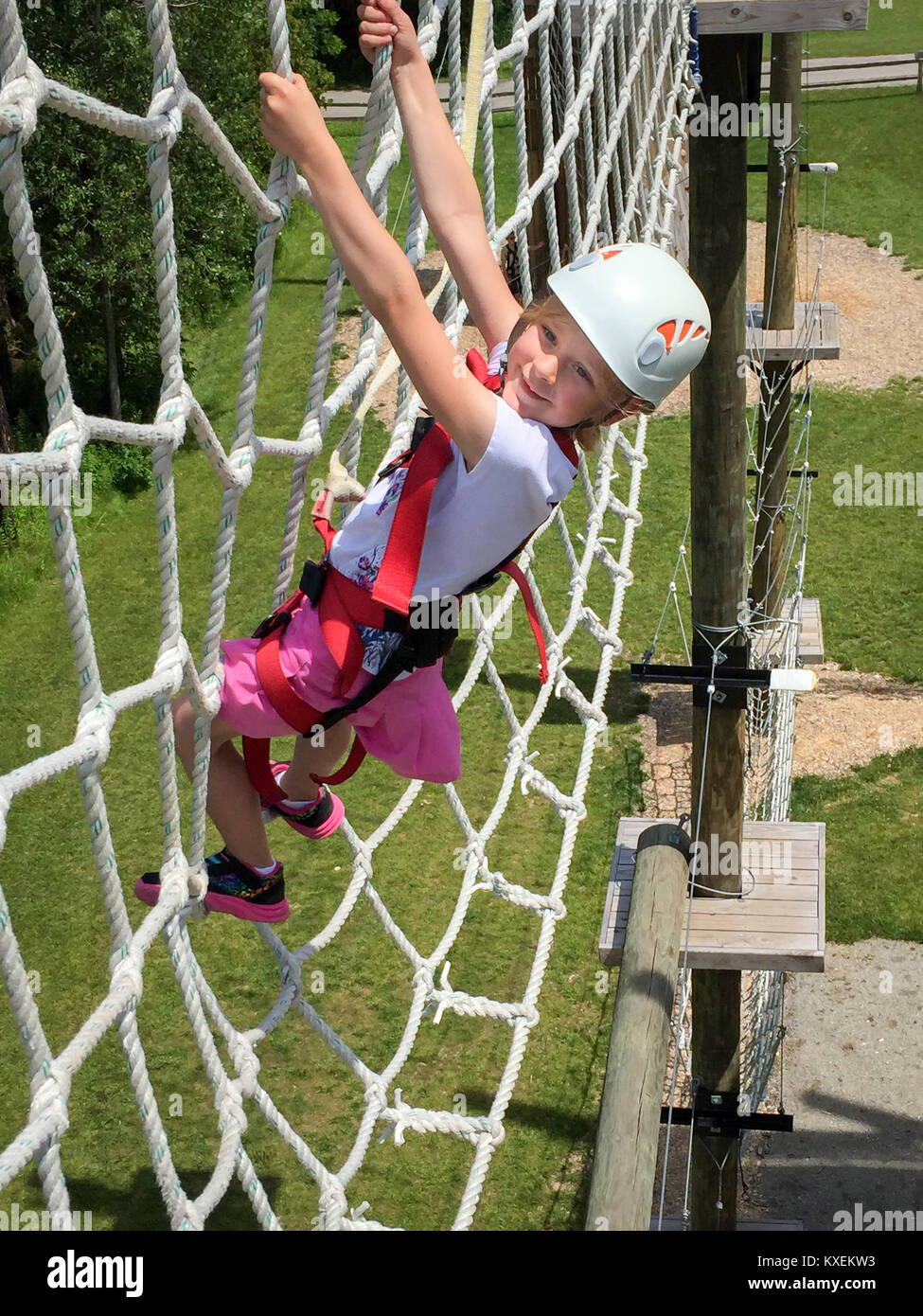 Wagemutige junge Mädchen klettern auf einer erhöhten Seil net auf ein Hindernis Kurs, Freude, Mut und Entschlossenheit. Stockfoto