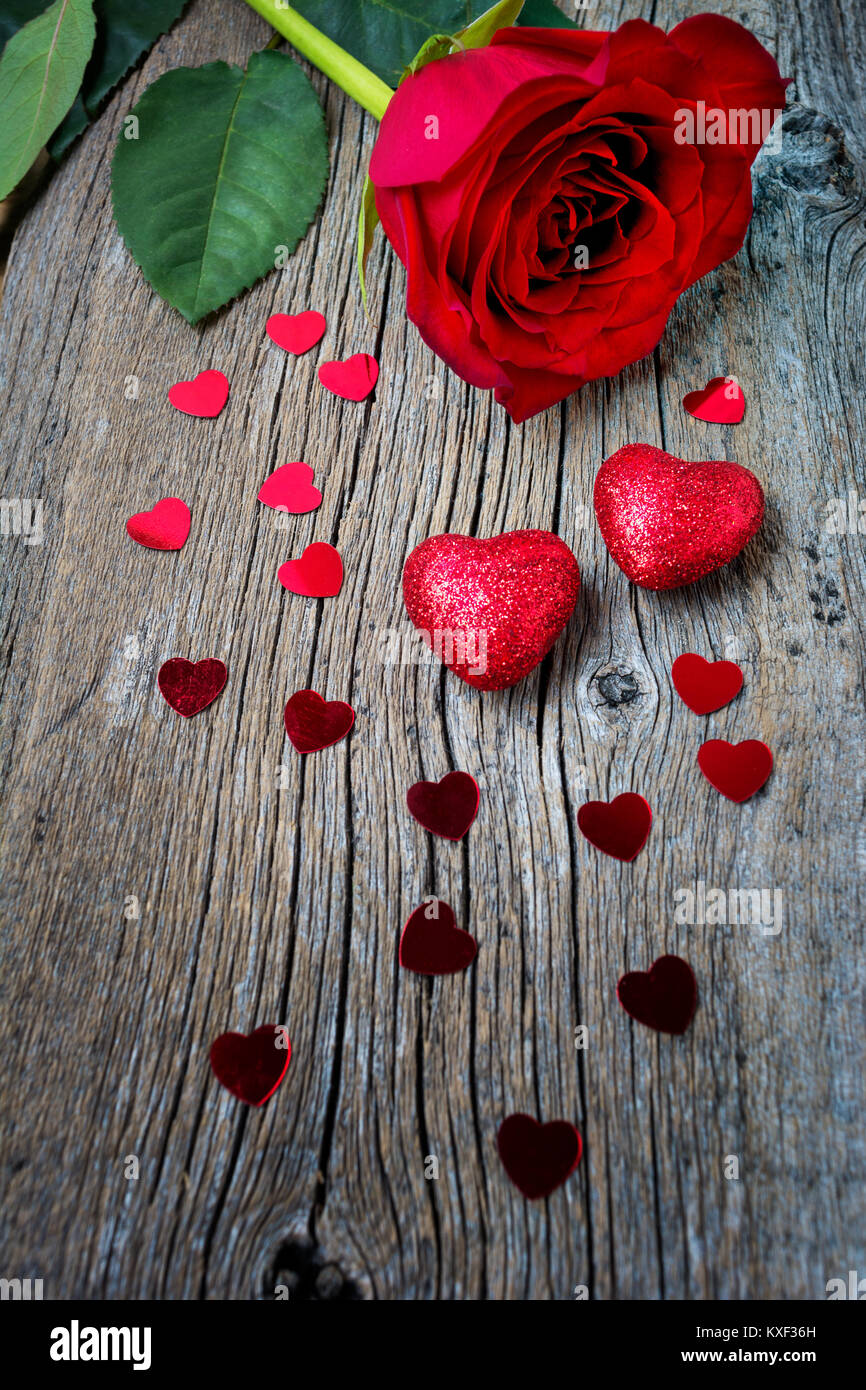 Valentines Tag oder Hochzeit Symbole eine rote Rose, Glitter und paillette Herzen auf dem rustikalen Holzmöbeln Hintergrund, kopieren. Stockfoto