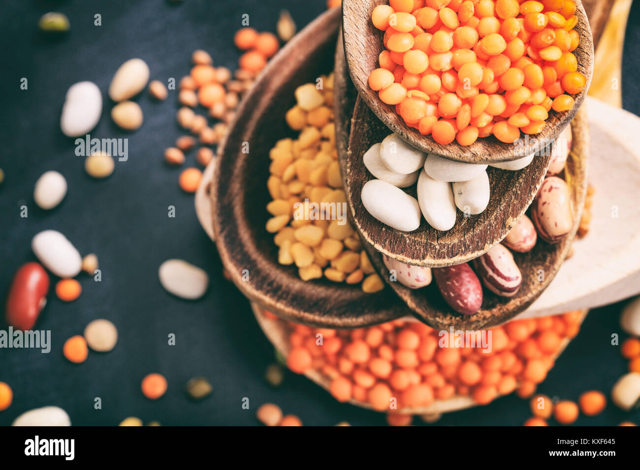 Verschiedene rohe Hülsenfrüchte in Holzlöffel auf schwarzem Hintergrund Stockfoto