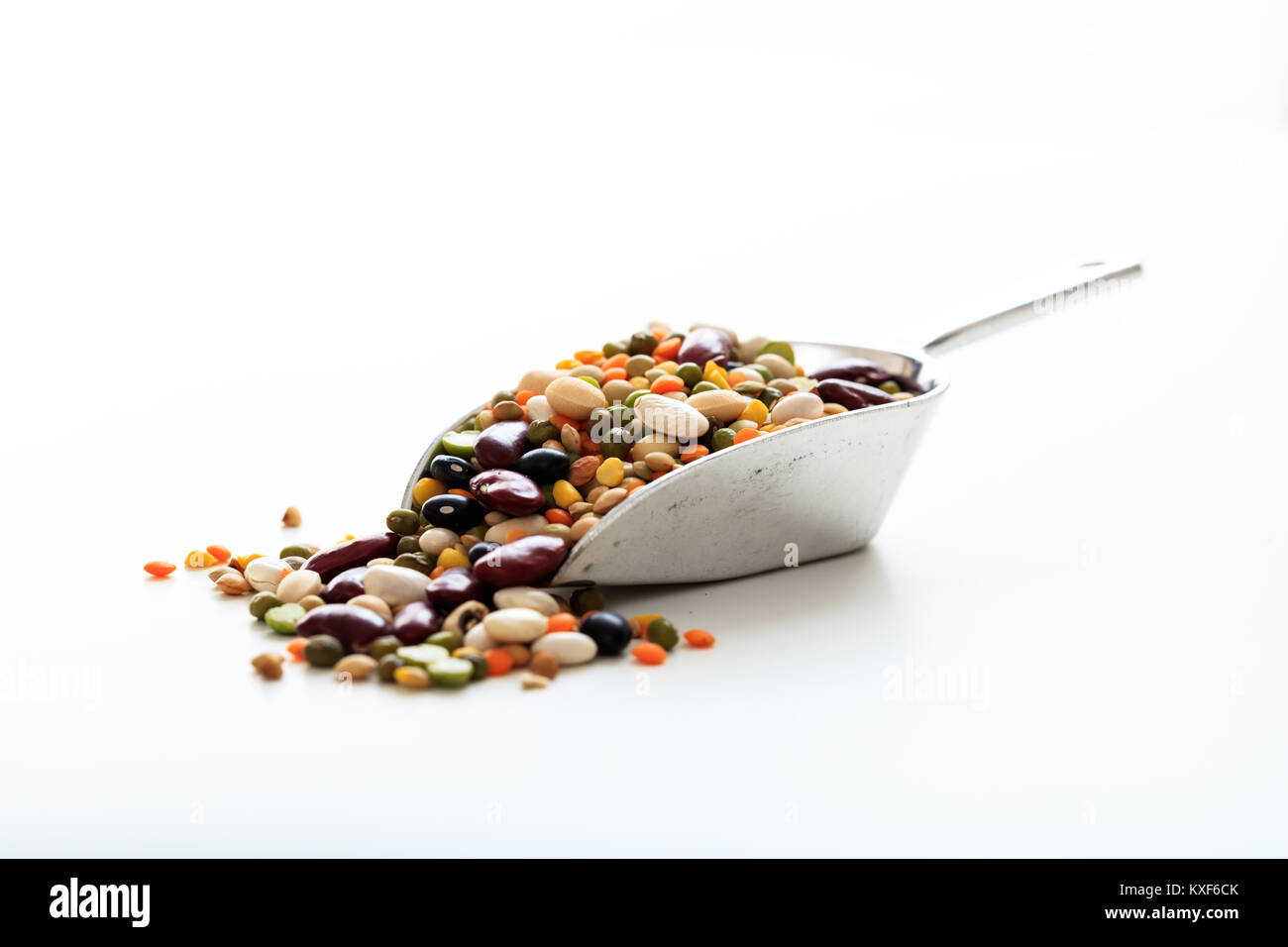Gemischte rohe Hülsenfrüchte in einer metallischen Kugel auf weißem Hintergrund Stockfoto