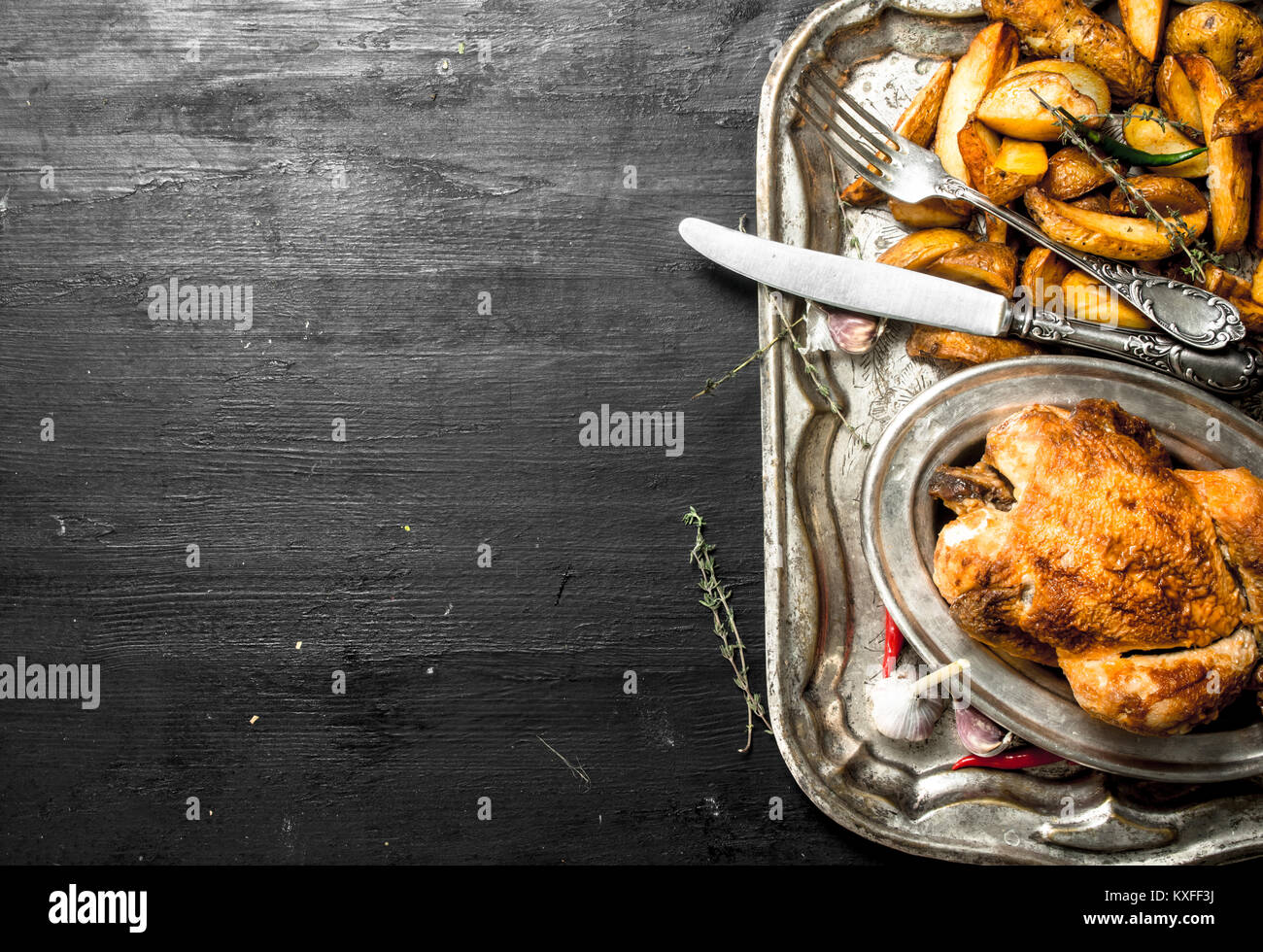 Gebratenes Huhn mit Kartoffeln auf ein Fach auf der schwarzen Tafel. Stockfoto
