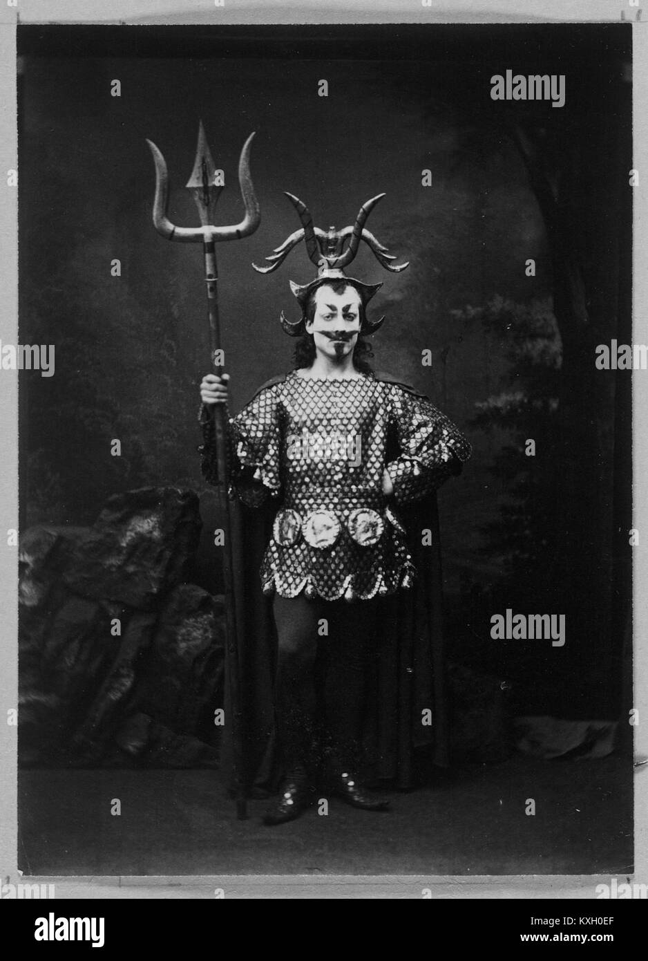 Ein Theaterfoto in der Sammlung Weir zeigt einen Schauspieler, der eine große Trident-Requisite in Kostümen hält, was eine klassische oder mythologische Rolle in der Bühnenaufführung andeutet. Stockfoto