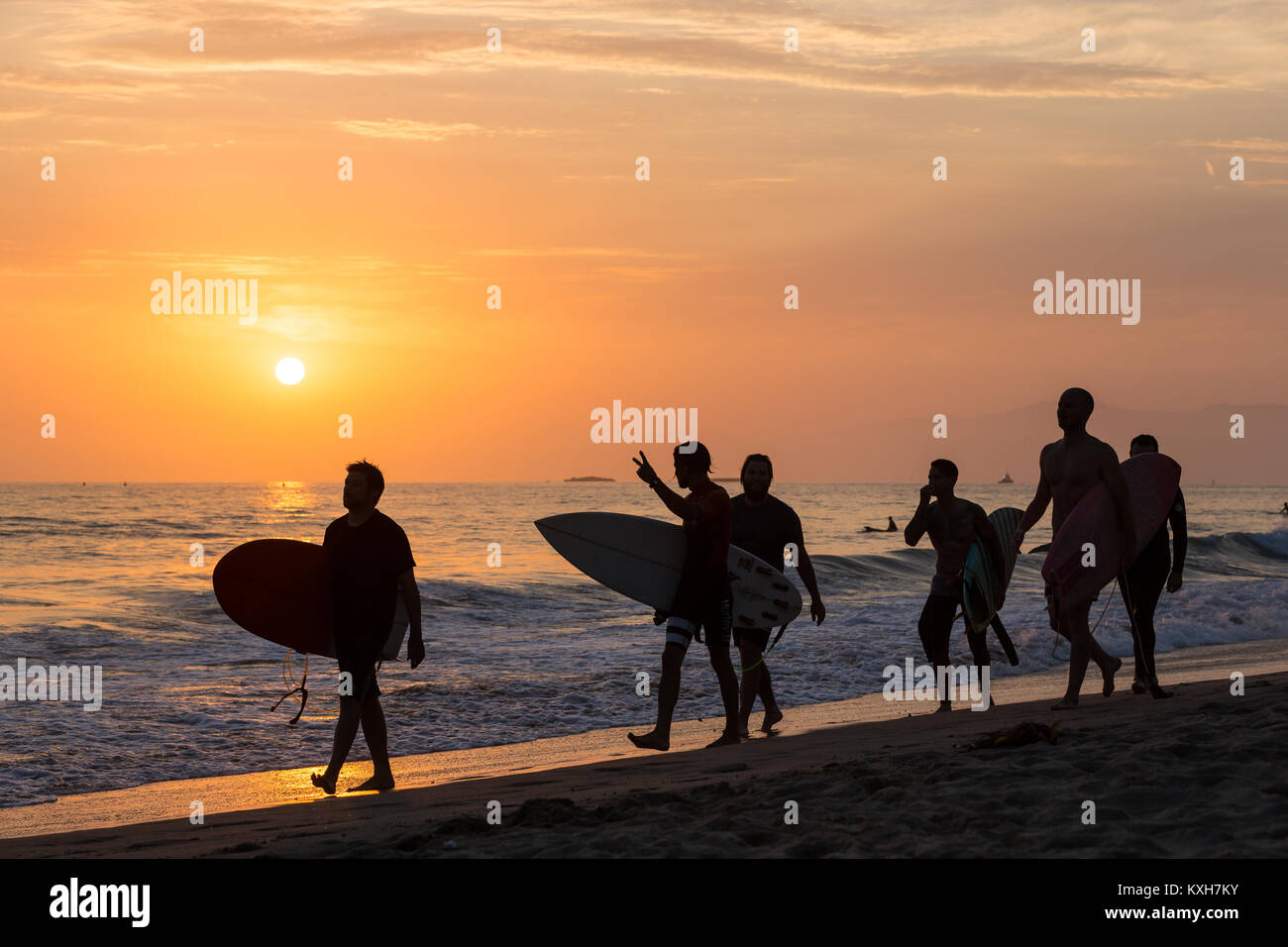 Eine Gruppe junger Surfer Spaziergänge über den Sand bei Sonnenuntergang in Los Angeles, Kalifornien. Stockfoto