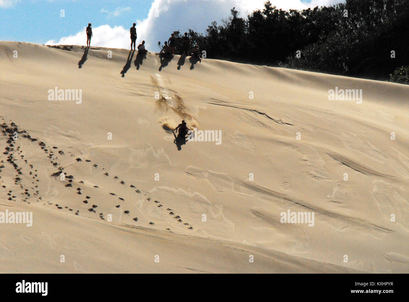 Silhouette einer Gruppe von nicht erkennbaren Kindern, die Spaß haben, indem sie eine riesige Sanddüne in Südafrika hinuntergleiten. Stockfoto