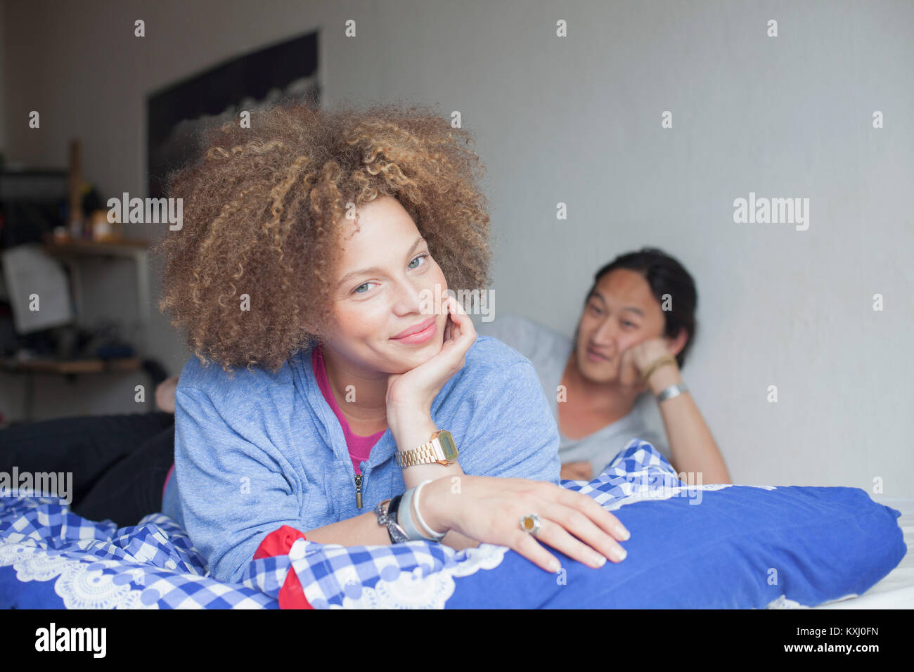 Porträt eines jungen Paares, das zu Hause mit den Händen am Kinn an der weißen Wand auf dem Bett liegt Stockfoto