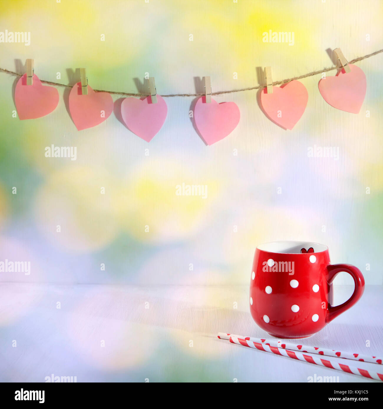 Red Cup, der mit einem weißen Punkt auf einem weißen Holztisch. Papier Herzen hängen an der Wand Stockfoto