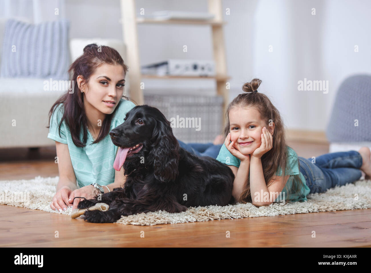 Porträt von Mutter und Tochter, die zu Hause mit Hund auf dem Teppich liegen Stockfoto