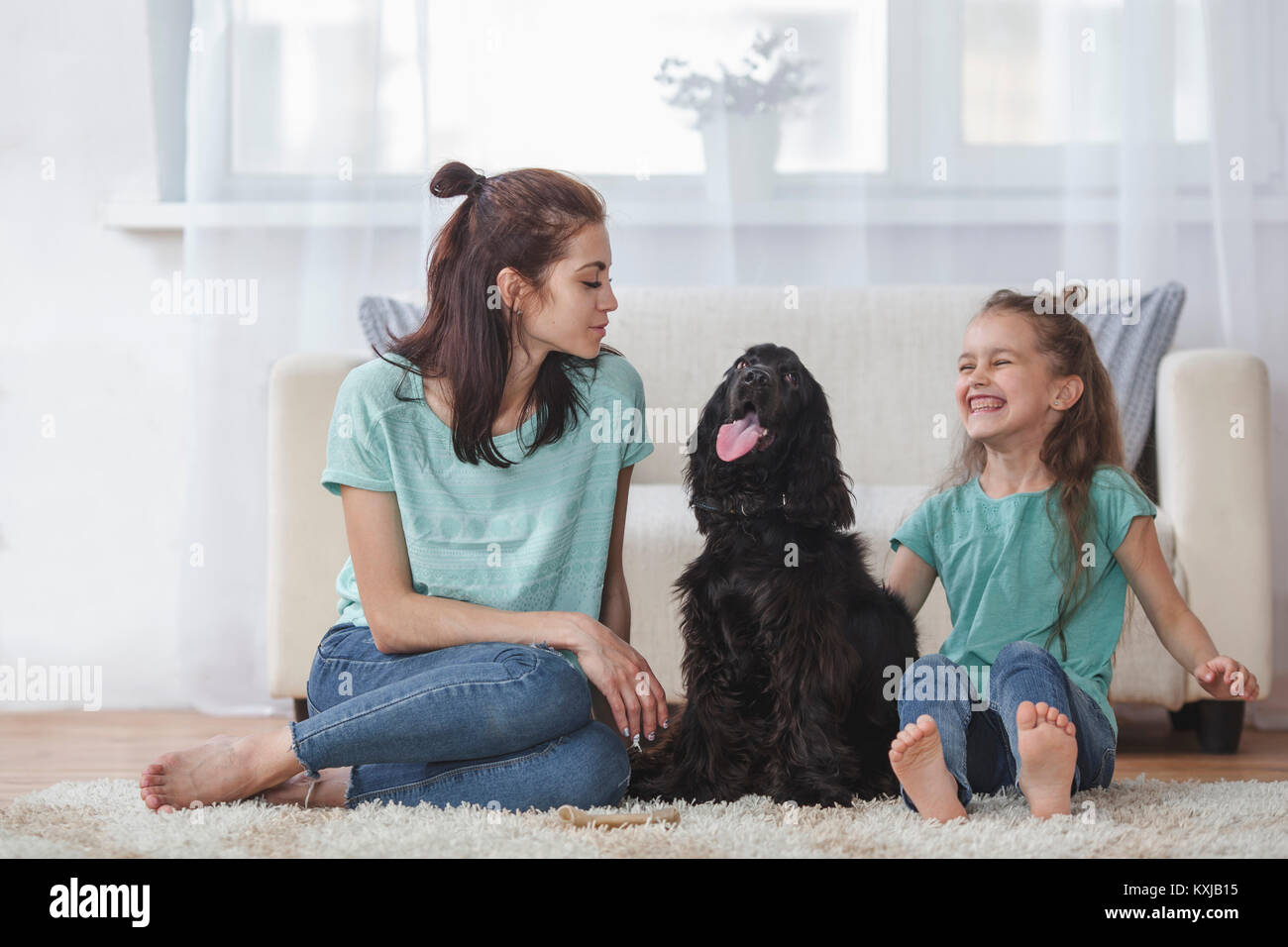 Fröhliches Mädchen, das von Cocker Spaniel und Mutter zu Hause im Wohnzimmer sitzt Stockfoto