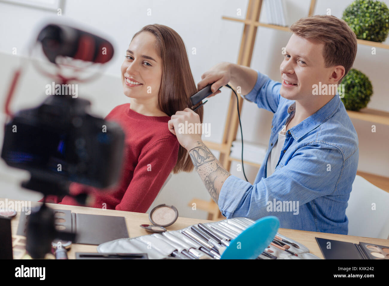 Emotionale Mann drücken die Haare von seinem Assistenten mit seinem lockenstab Stockfoto