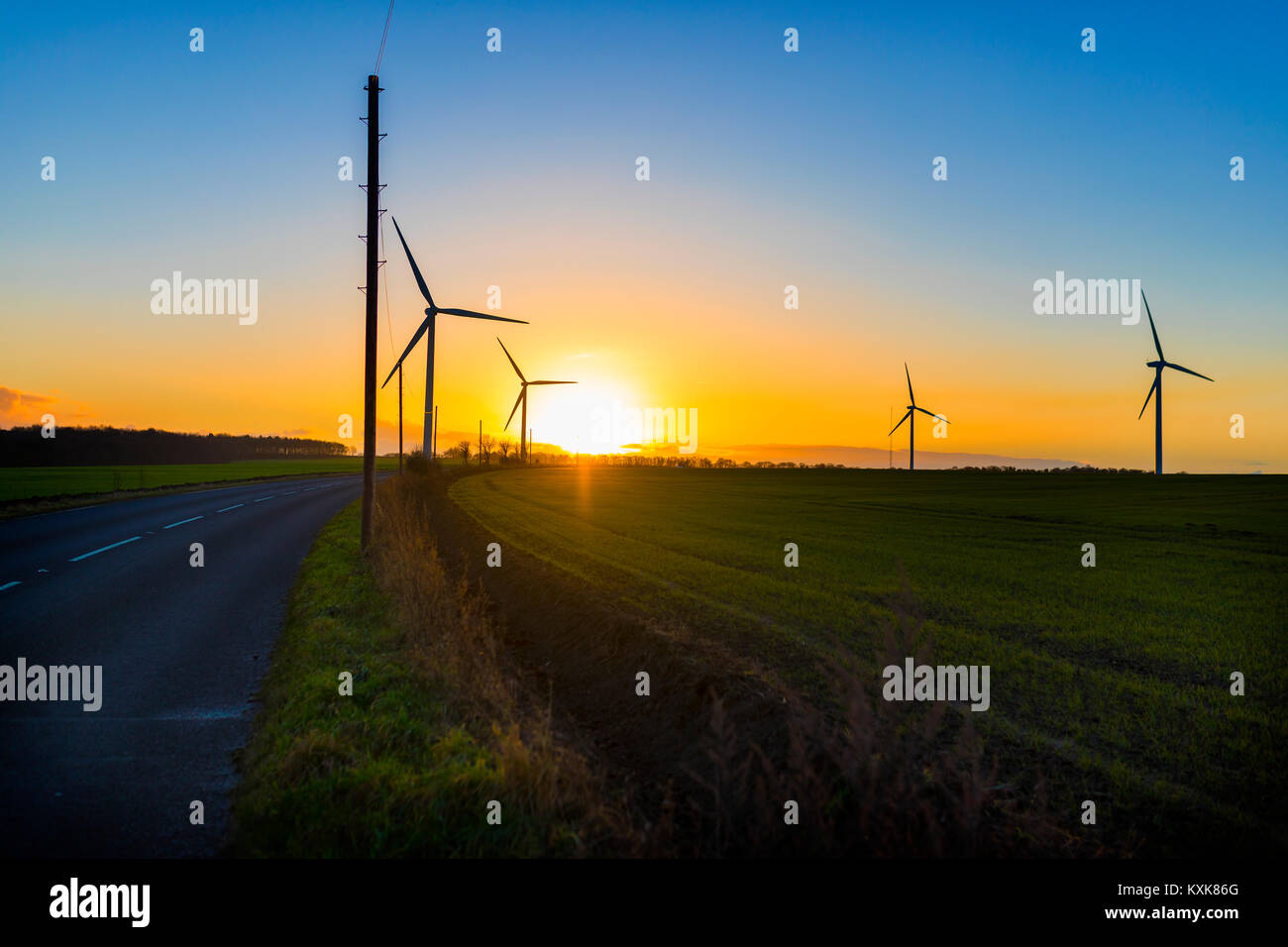 Land straße, die Windenergieanlagen in einem Gebiet in Großbritannien bei Sonnenuntergang oder Sunrise gegen einen klaren Himmel, Wind Stockfoto