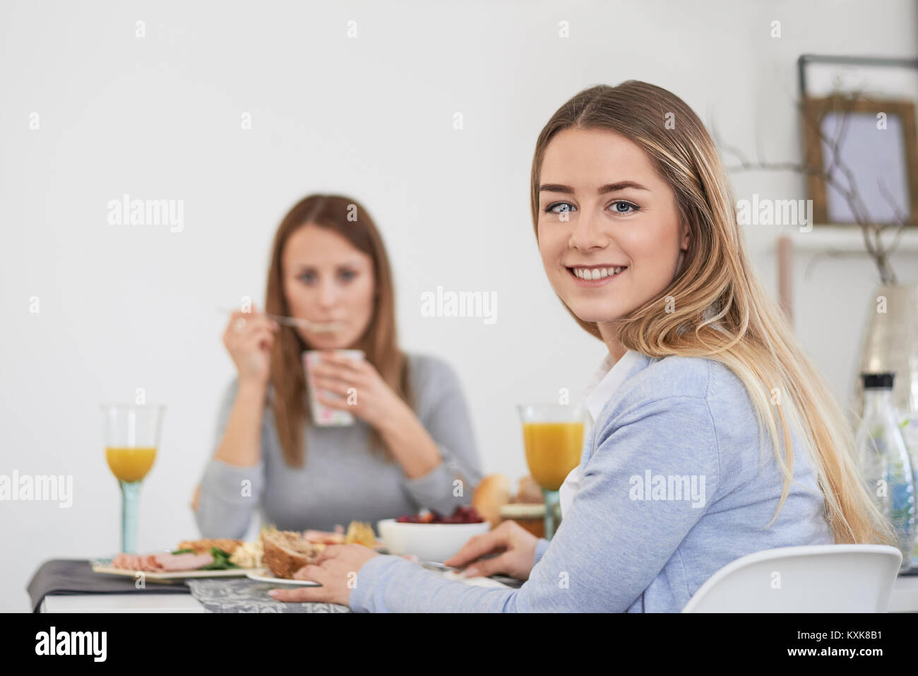 Hübsche junge Teenager Frau mit einem temperamentvollen Lächeln an einem Tisch sitzen mit Ihrer besten Freundin genießen Sie Frühstück und Drehen in die Kamera Stockfoto