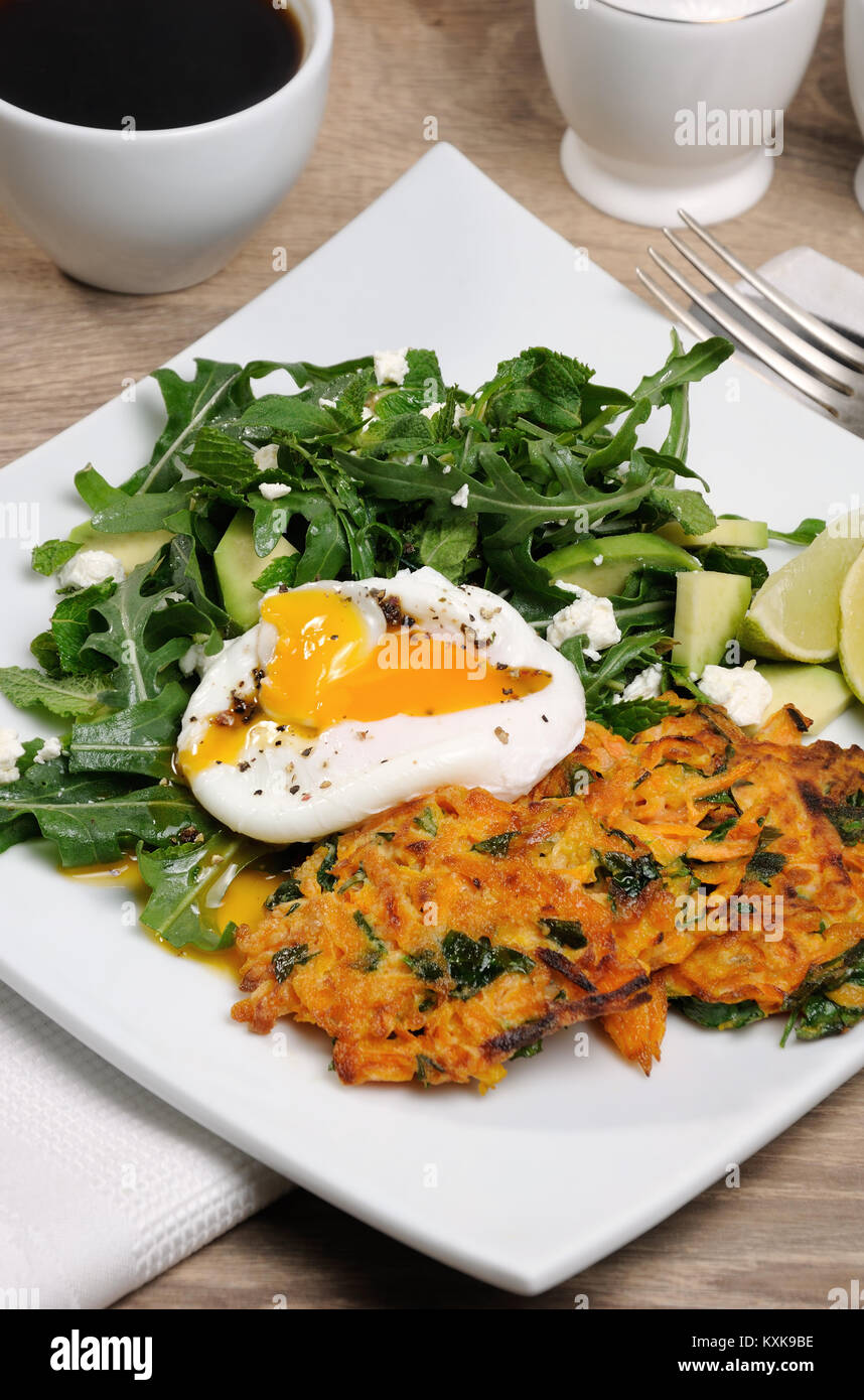 Brunch-Idee. Pochiertes Ei mit Kürbis-Spinat-Pfannkuchen und Garnitur aus Rucola, Avocado, Minze und ricotta Stockfoto