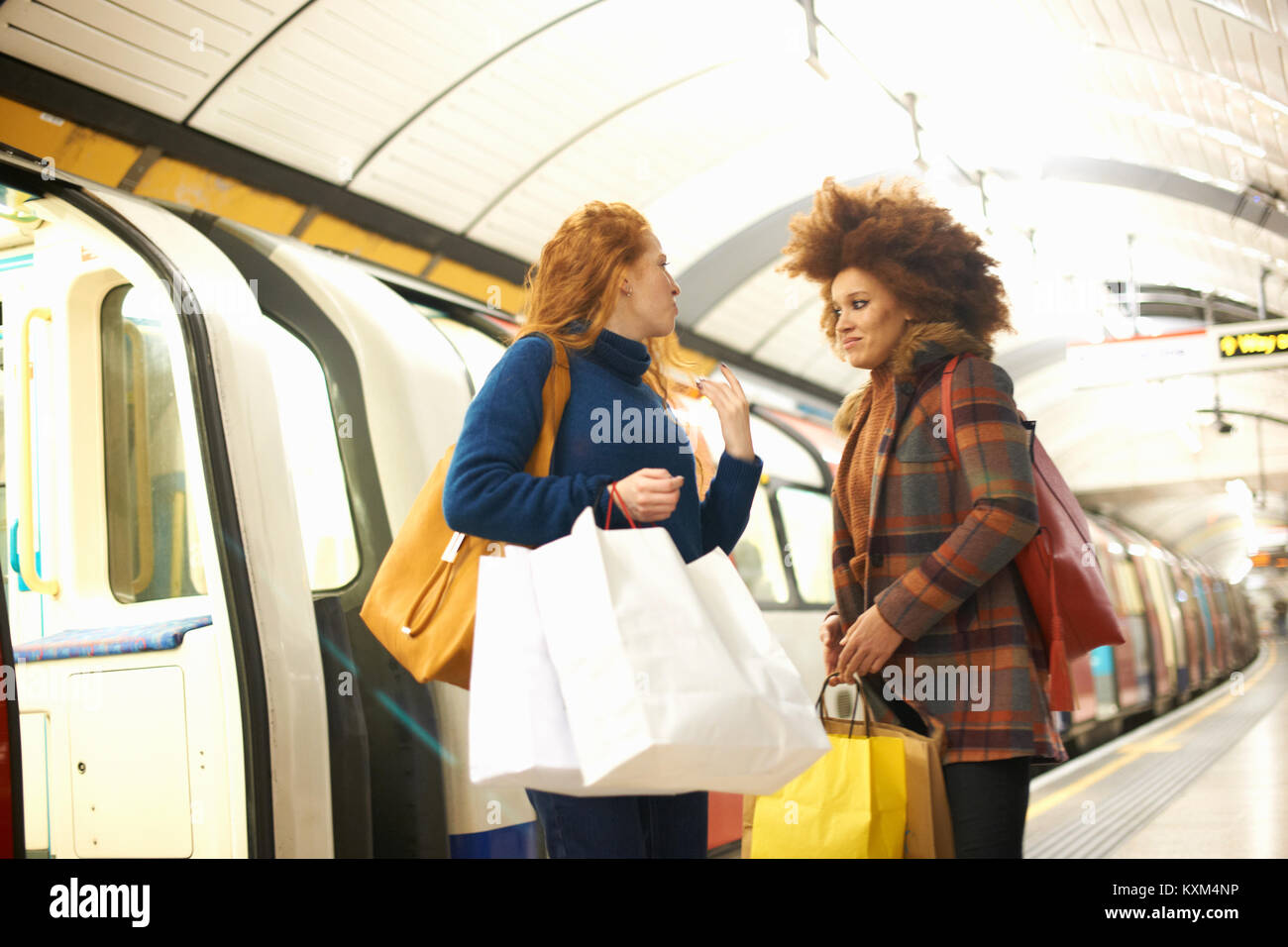 Zwei junge Frauen, die auf der U-Bahn, Plattform, holding Shopping Taschen Stockfoto