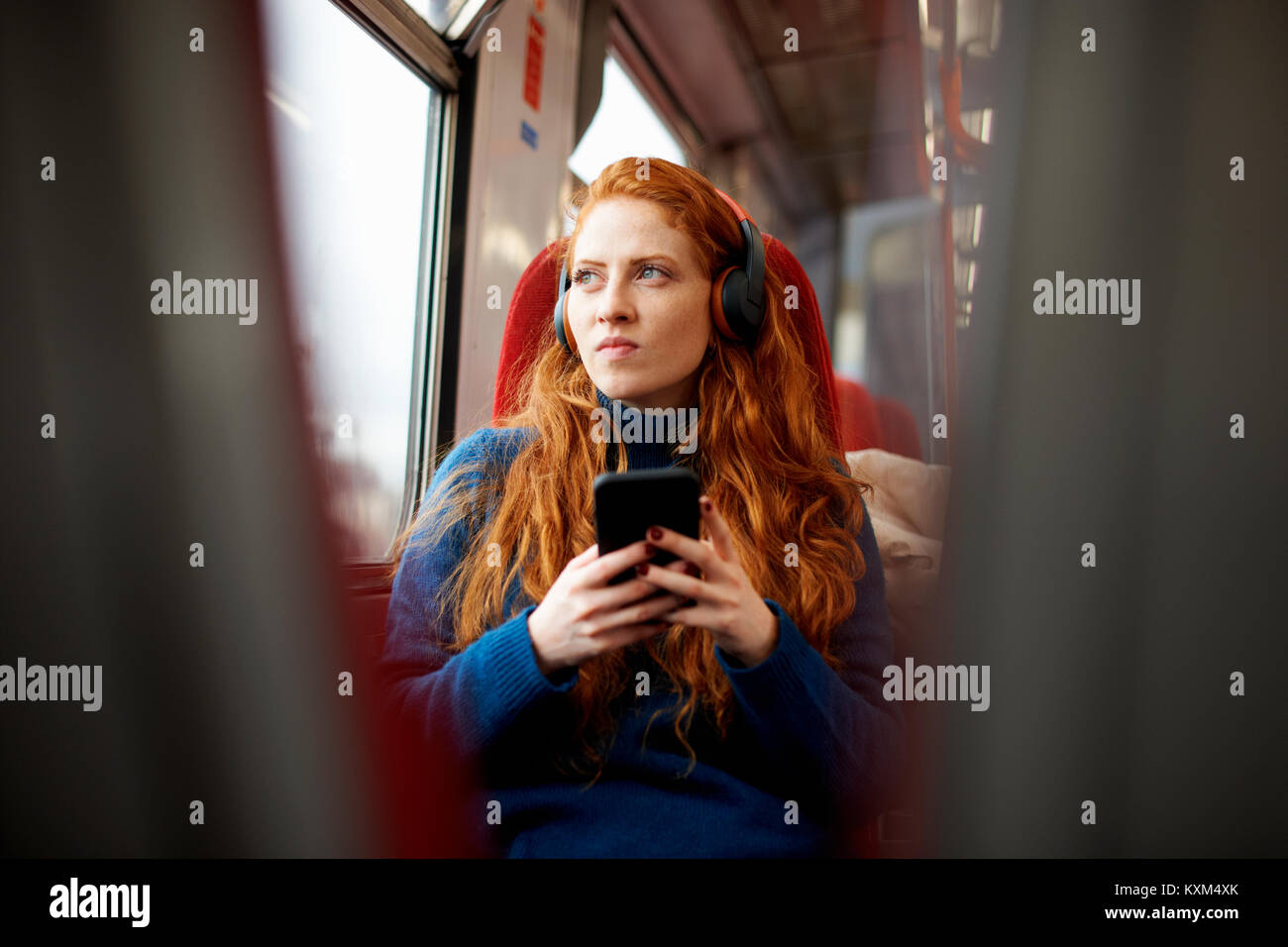Frau auf dem Zug hören die Musik auf Handy mit Kopfhörer, London Stockfoto