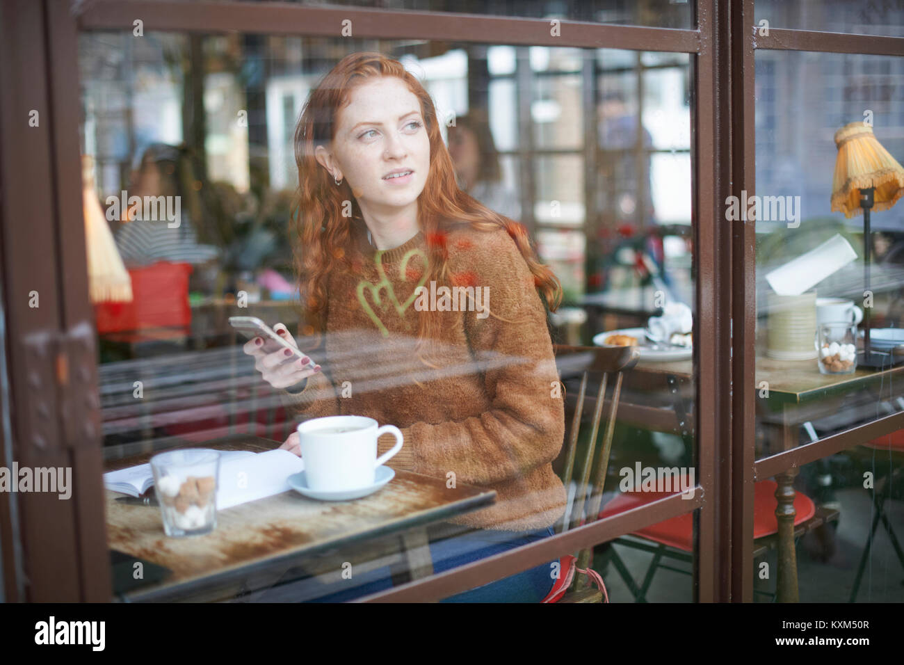 Blick durch das Fenster der Frau im Café mit Handy Stockfoto