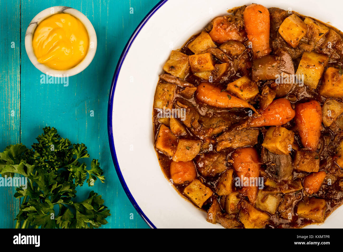 Rindfleisch und Rotwein Auflauf mit Braten Kartoffeln Karotten und Pilzen vor einem blauen Hintergrund Stockfoto