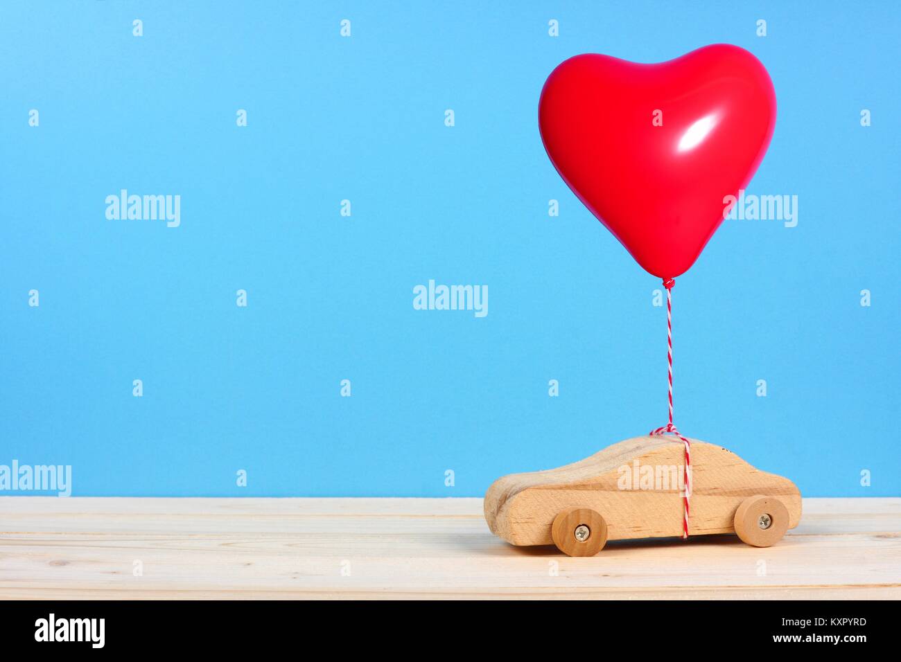 Holzspielzeug Auto mit einem roten Herz Ballon vor einem blauen Hintergrund. Valentines Tag oder Liebe Konzept. Stockfoto