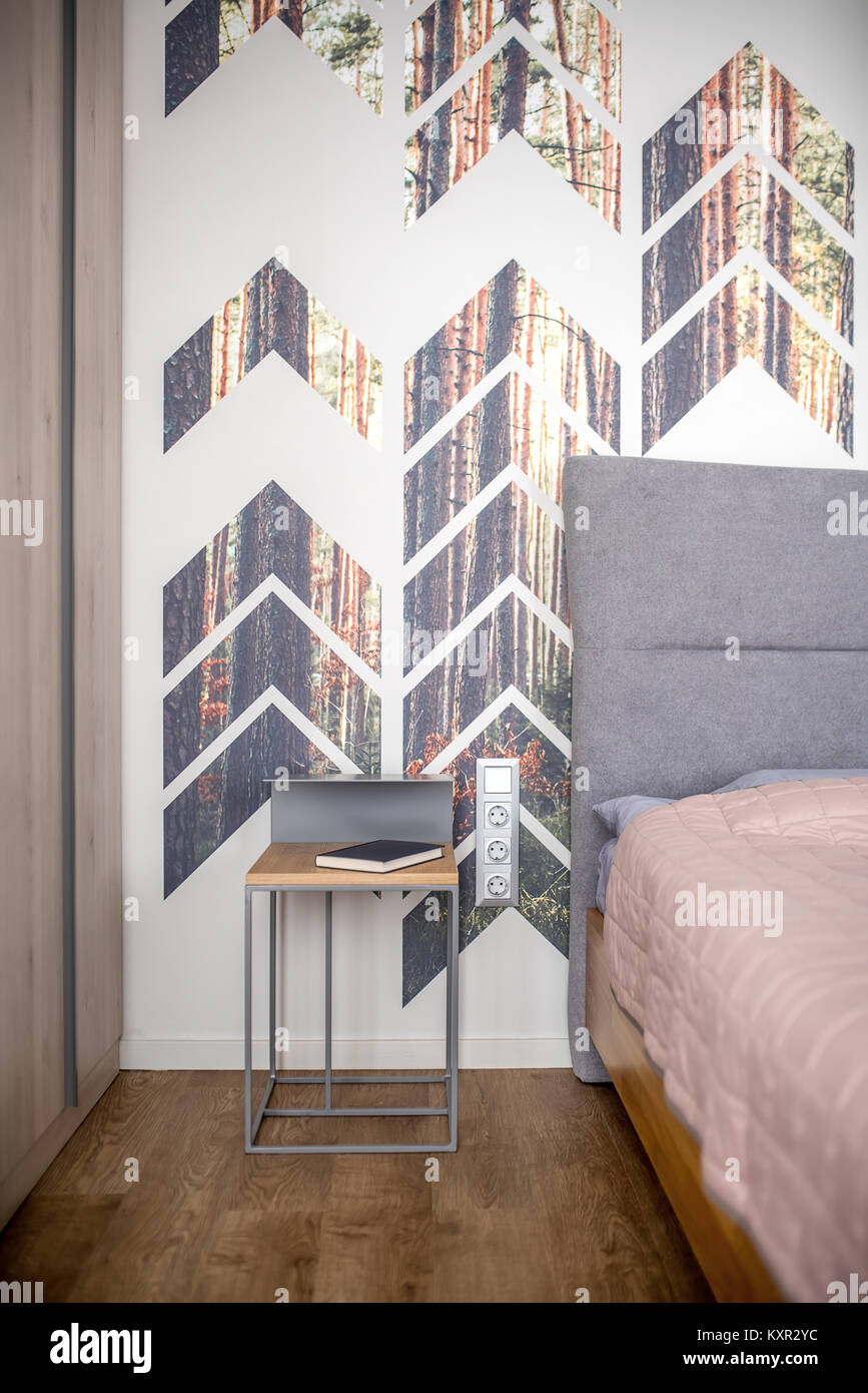 Modernes Schlafzimmer mit einem bunten Wand mit Kiefer gedruckt wird. Es ist ein Bett mit einem Pfirsich Bettdecke und eine graue Kissen, Metall - holz Nachttisch mit einem Boo Stockfoto
