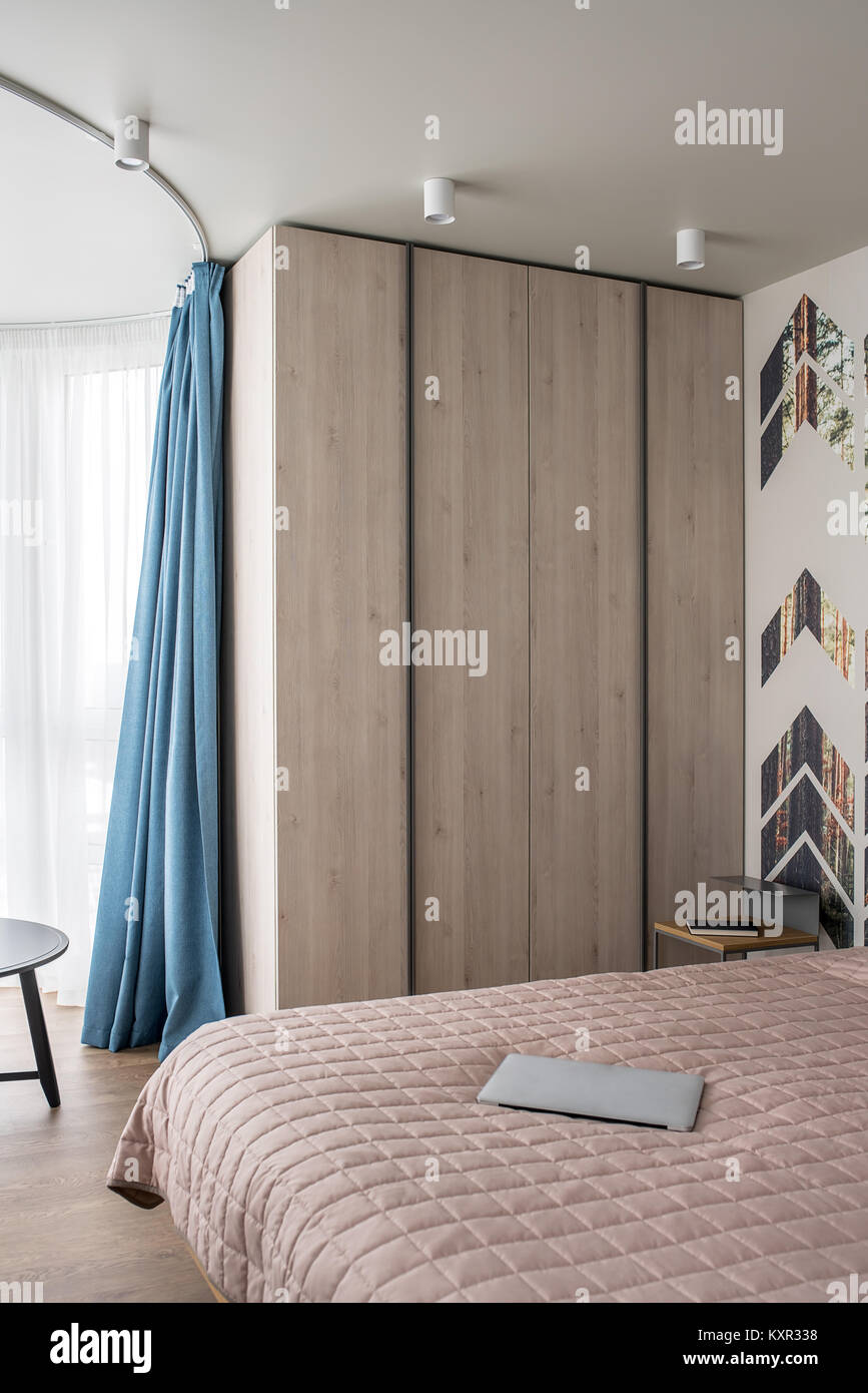 Modernes Schlafzimmer mit einem bunten Wand mit Kiefer gedruckt wird. Es gibt ein Bett mit einer Bettdecke und ein Laptop, Nachttisch mit einem Buch, Schließfach, dunkle r Stockfoto