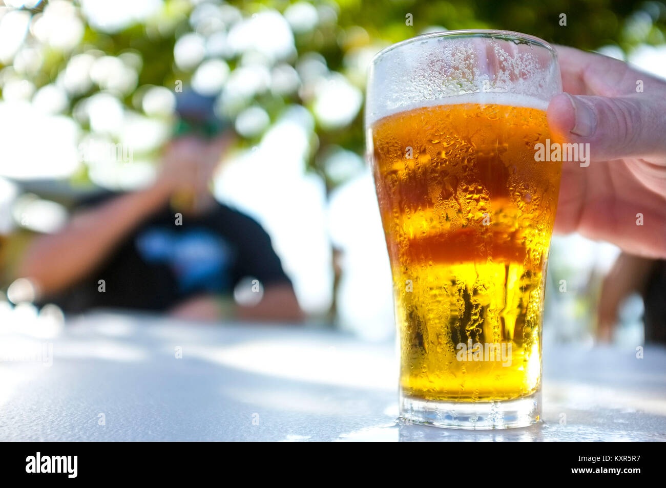 Des Menschen Hand packte einen Glas Bier an einem Tisch im Freien. Stockfoto
