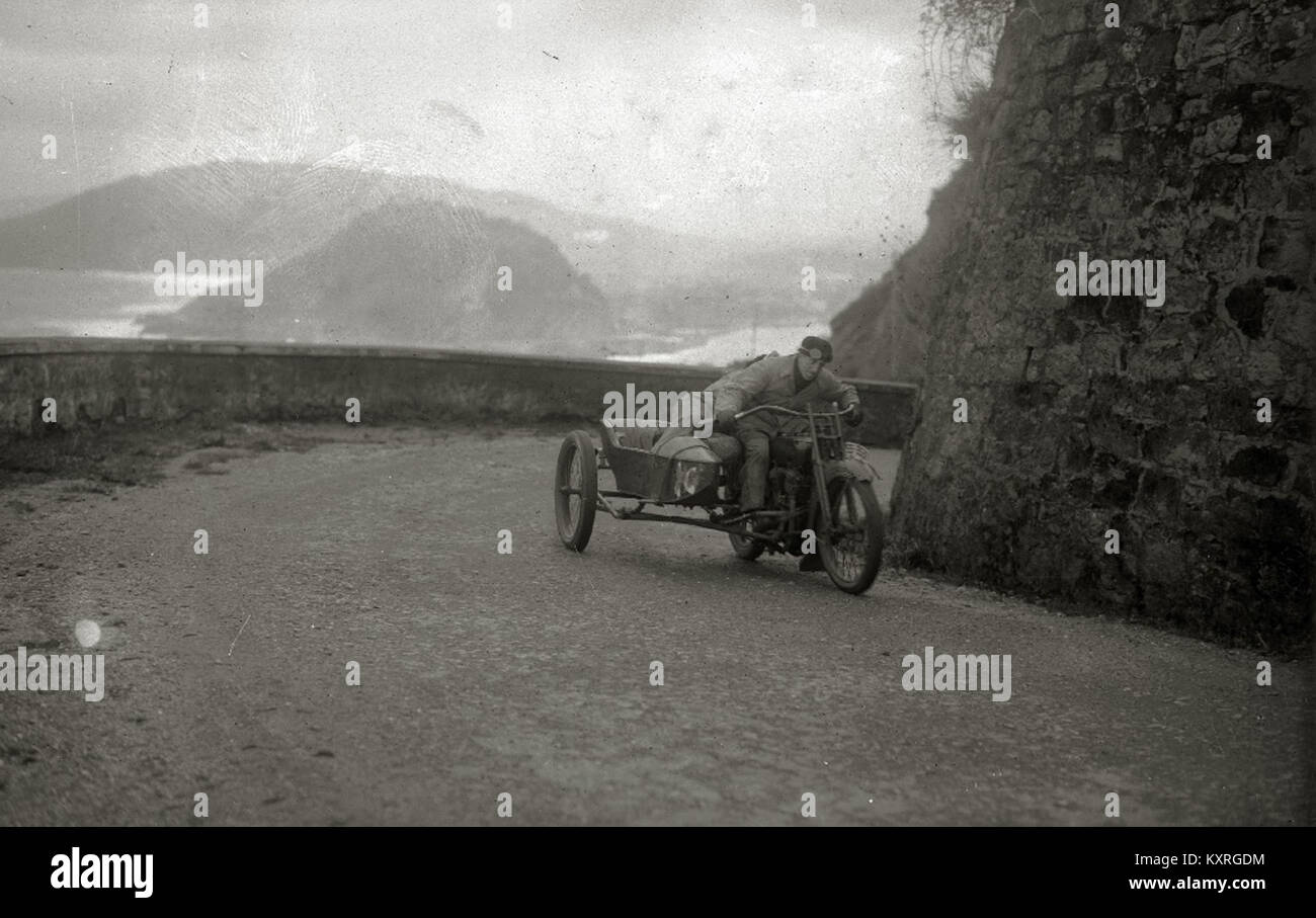 Dieses historische Foto zeigt ein Auto- und Motorradrennen, das auf dem Paseo del Faro ausgetragen wurde und das frühe Motorsport in Spanien zeigt, bei dem Fahrzeuge entlang einer Küstenpromenade fahren. Stockfoto