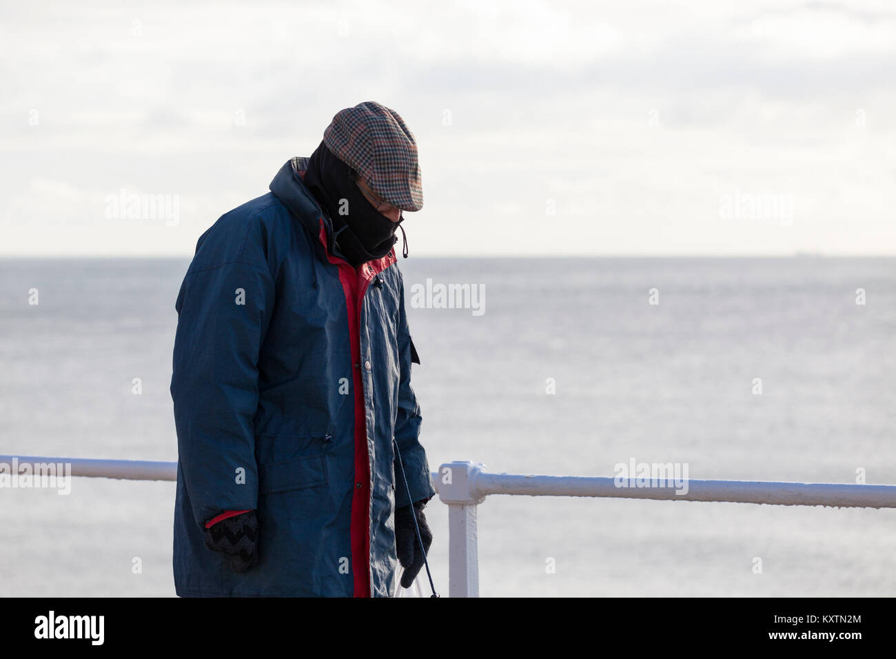 Ein Mann warm eingepackt für den Winter Spaziergänge entlang der Strandpromenade von Hastings, East Sussex Stockfoto