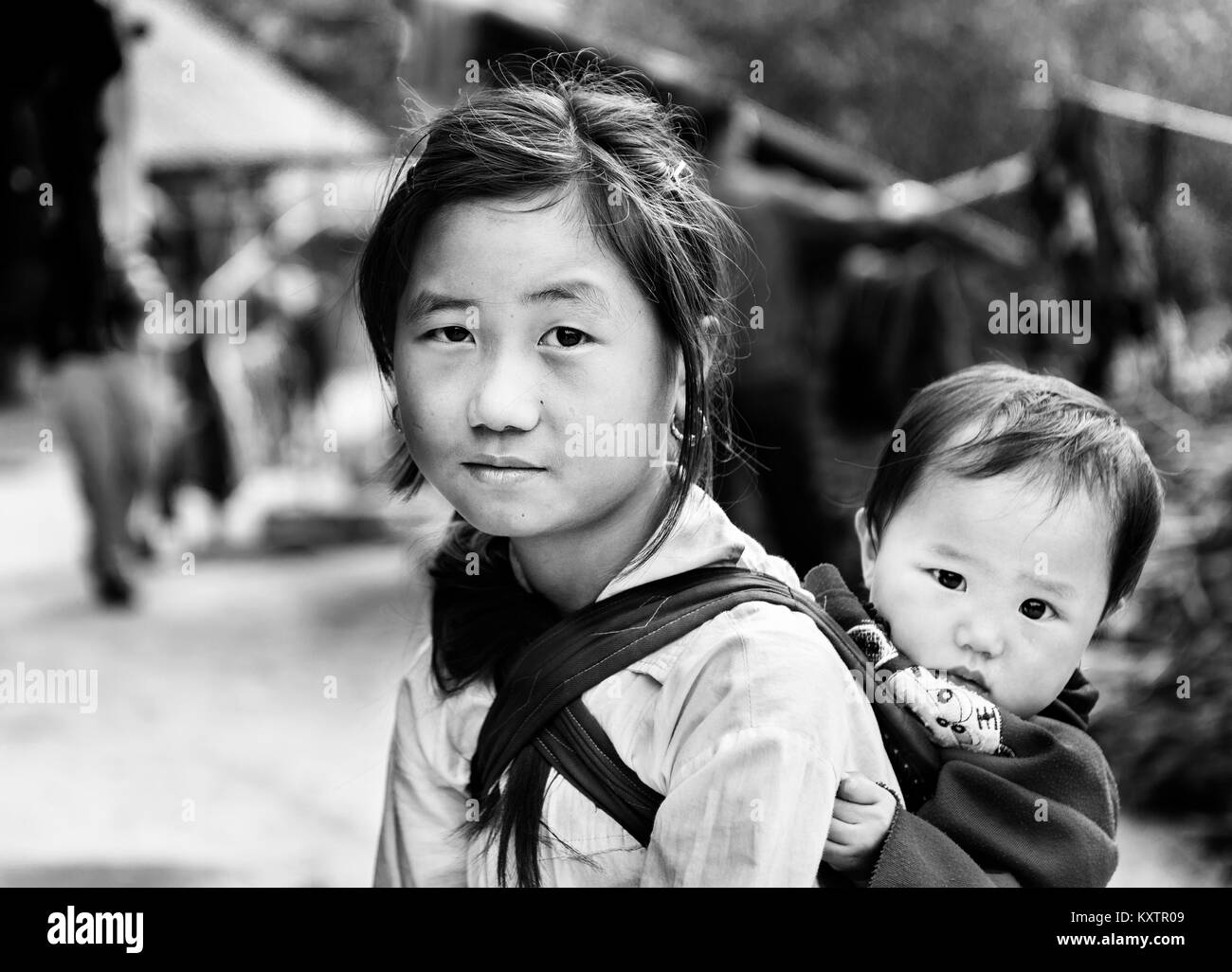 Kleines Mädchen ihren Bruder, die hinter den Schultern, bis ihre Mutter von der Arbeit kommen, Vietnam Stockfoto