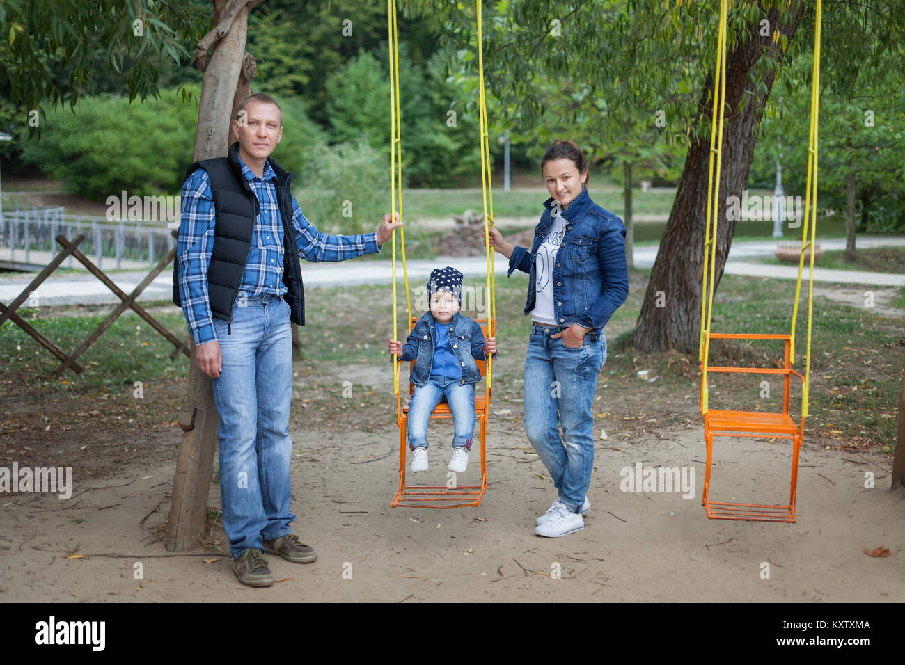 Papa und Mama roll ihre Tochter auf einer Schaukel im Park. Stockfoto