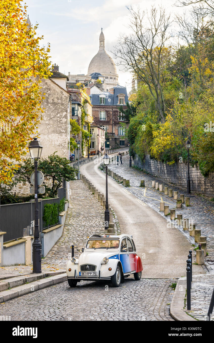 Ein französischer Oldtimer aus dem Citroën 2CV, der eine Straße von Montmartre in Paris, Frankreich, entlang fährt, mit der Basilika des Heiligen Herzens im Hintergrund. Stockfoto