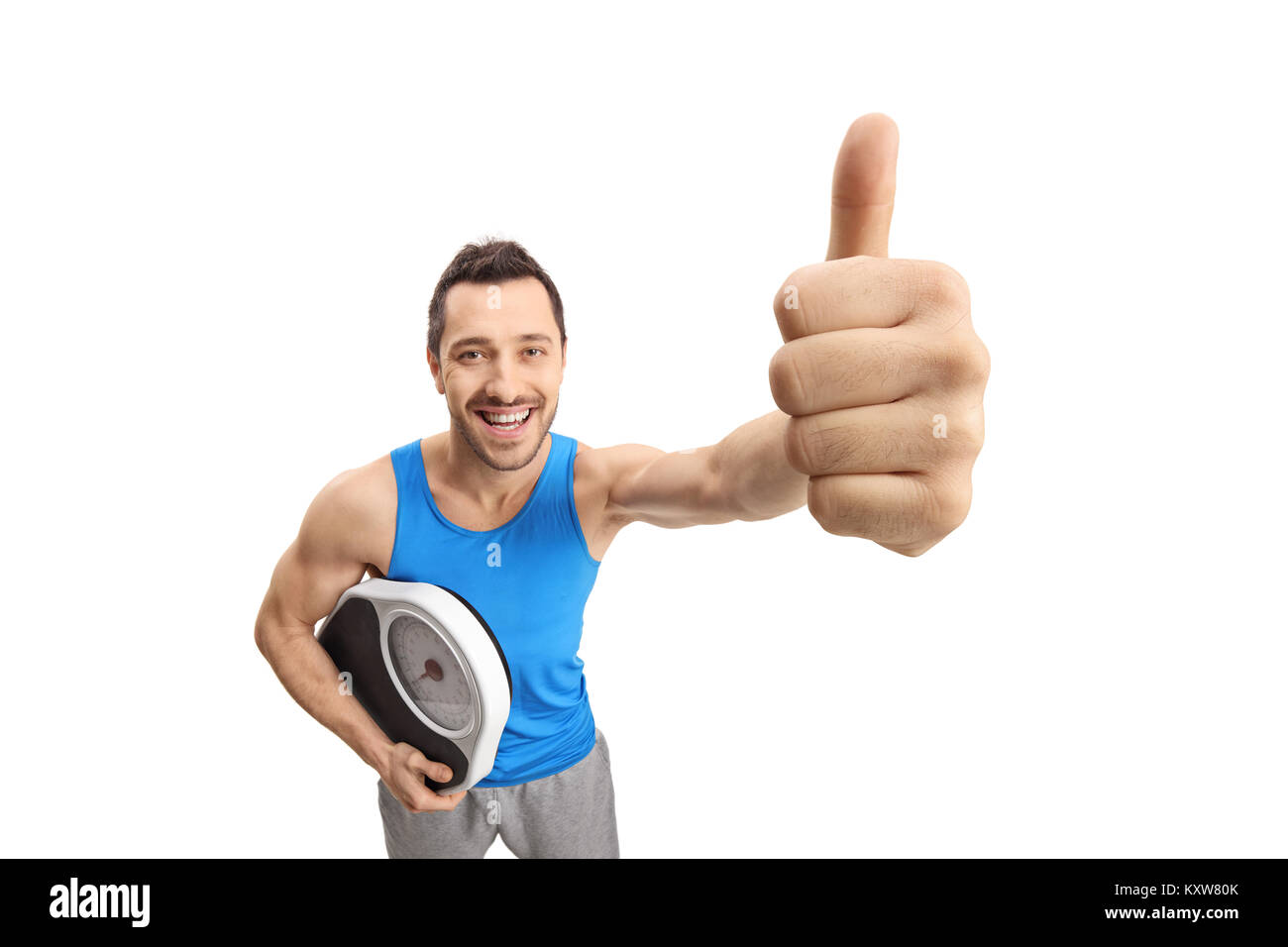 Junge Mann in Sportkleidung Holding eine Waage und ein "Daumen hoch" Geste auf weißem Hintergrund Stockfoto