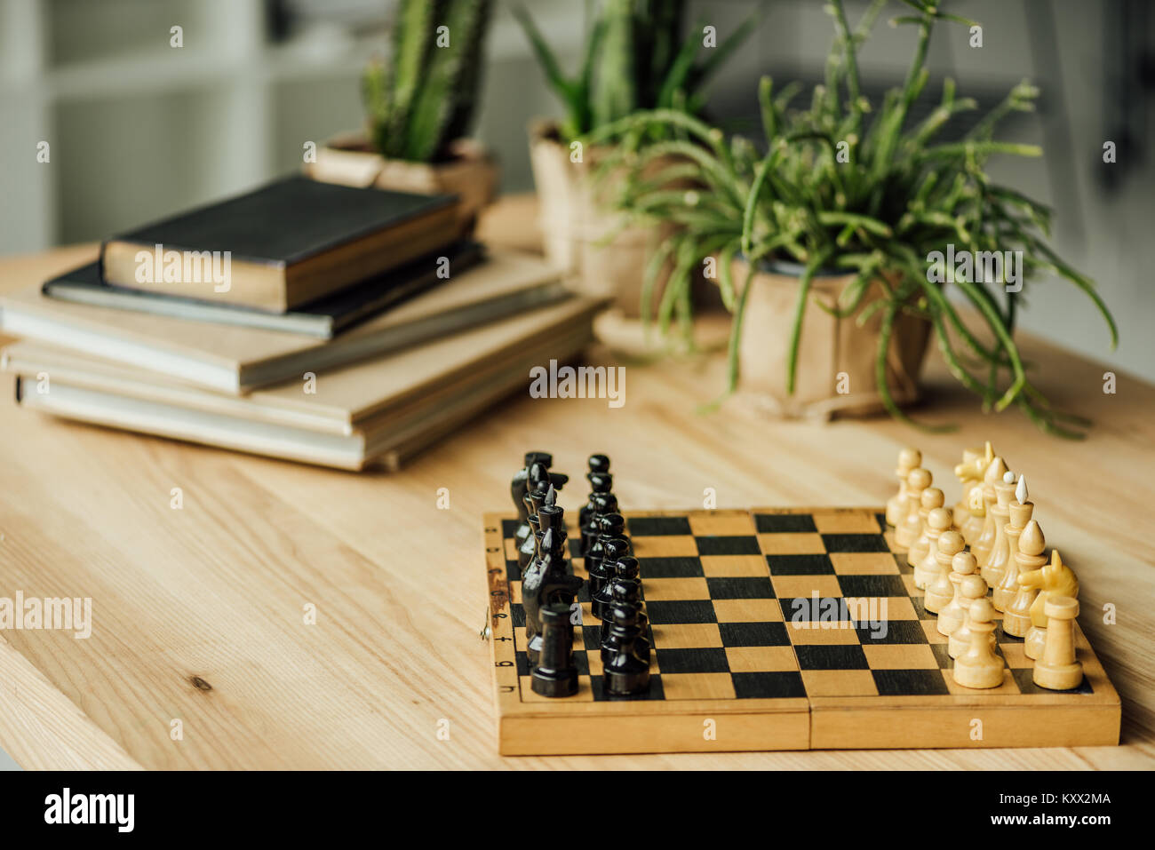 Schachbrett für ein neues Spiel auf dem Tisch mit Büchern und Topfpflanzen eingerichtet Stockfoto