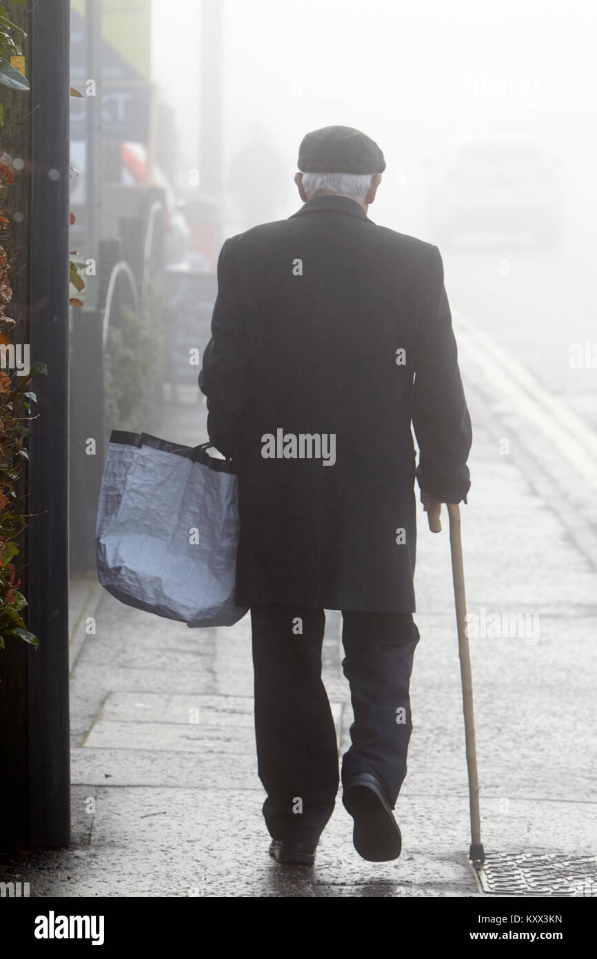 Älterer Mann mit Stock und Shopping Bag Walking Street auf nebligen Tag in Großbritannien Stockfoto