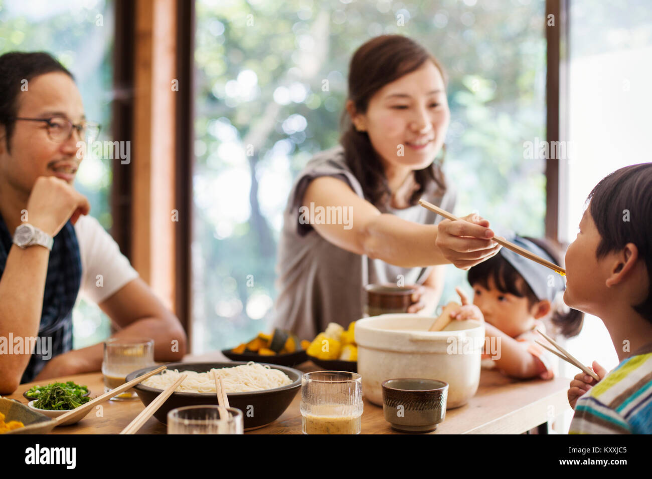 Mann, Frau und Jungen sitzen um einen Tisch mit Schüsseln mit Essen, essen. Stockfoto
