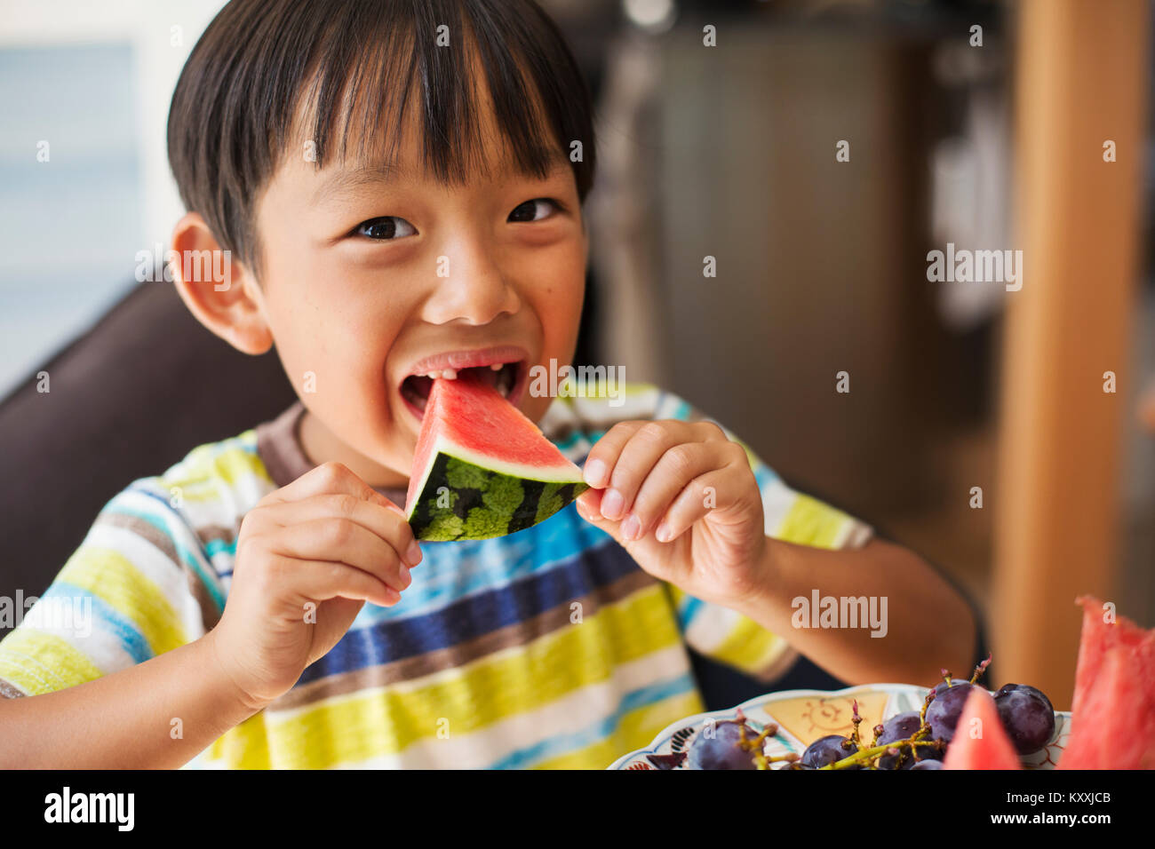 Der Junge mit den schwarzen Haaren tragen gestreifte T-Shirt essen ein Stück Wassermelone. Stockfoto