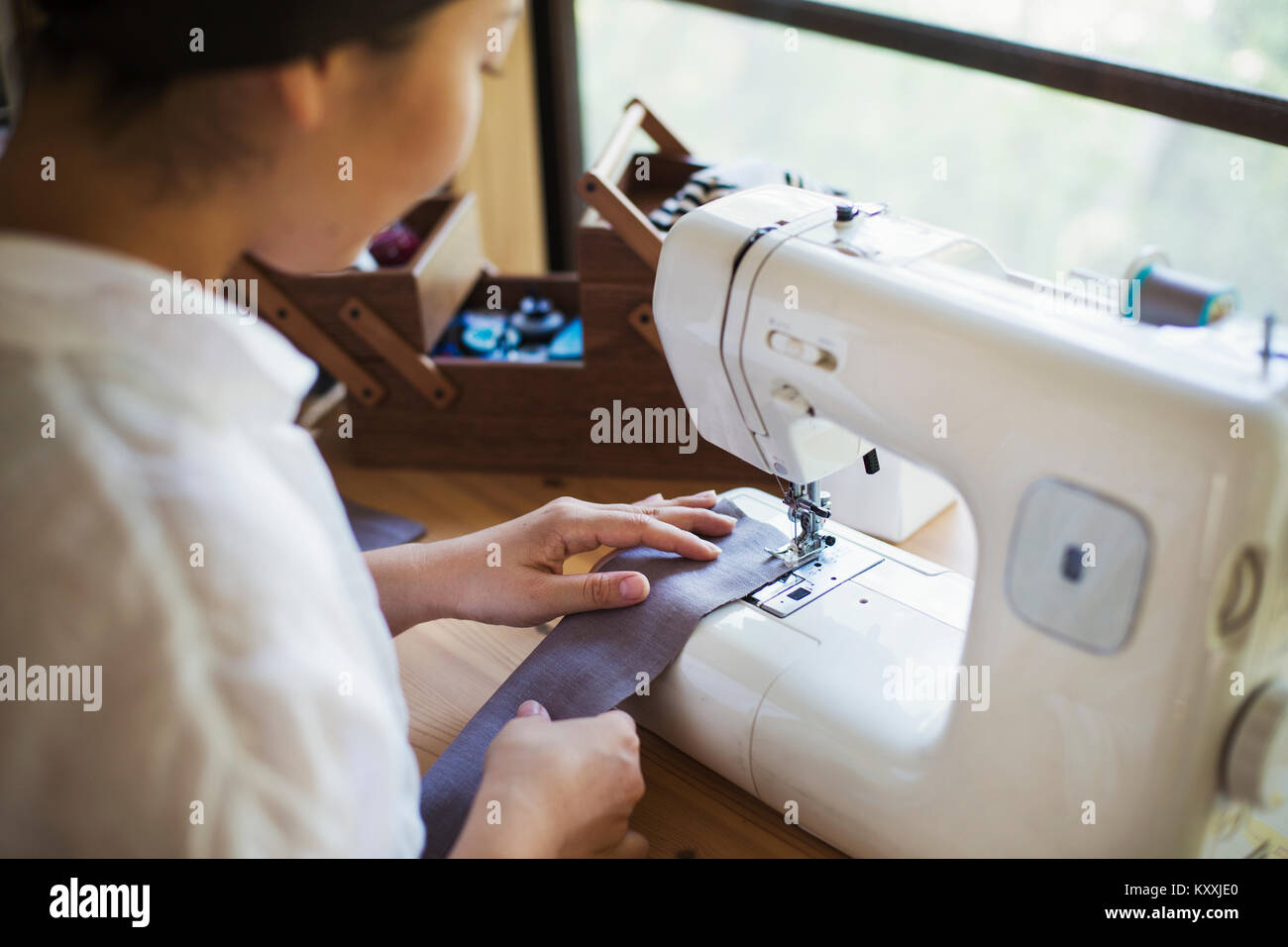 Nahaufnahme von Frau sitzt an einer Nähmaschine, Nähen grauen Streifen Stoff. Stockfoto