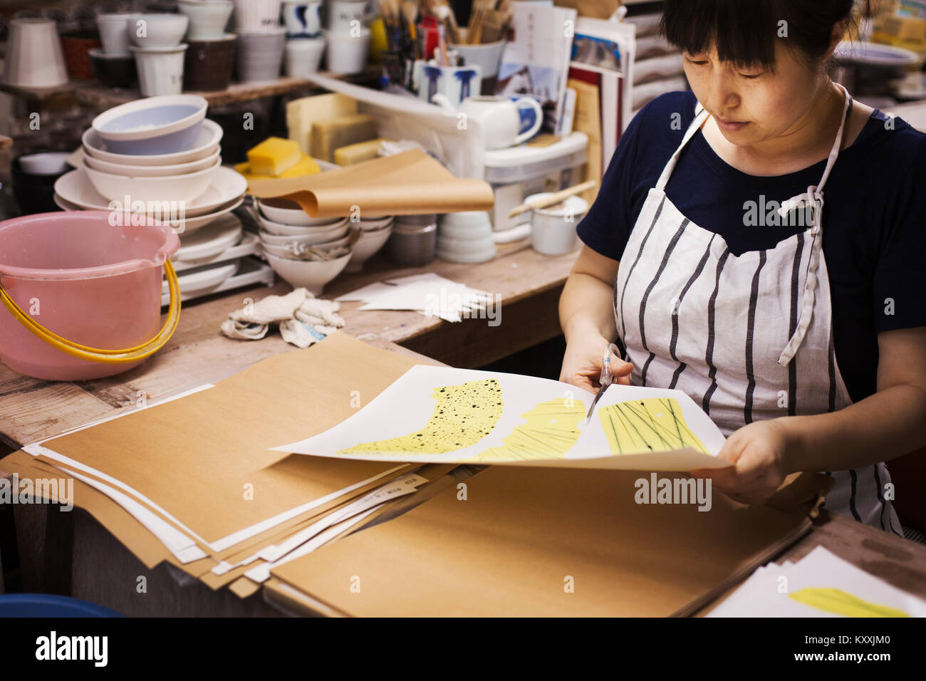 Frau sitzt in einem japanischen Porzellan Werkstatt, Ausschneiden von Design Patterns mit einer Schere. Stockfoto