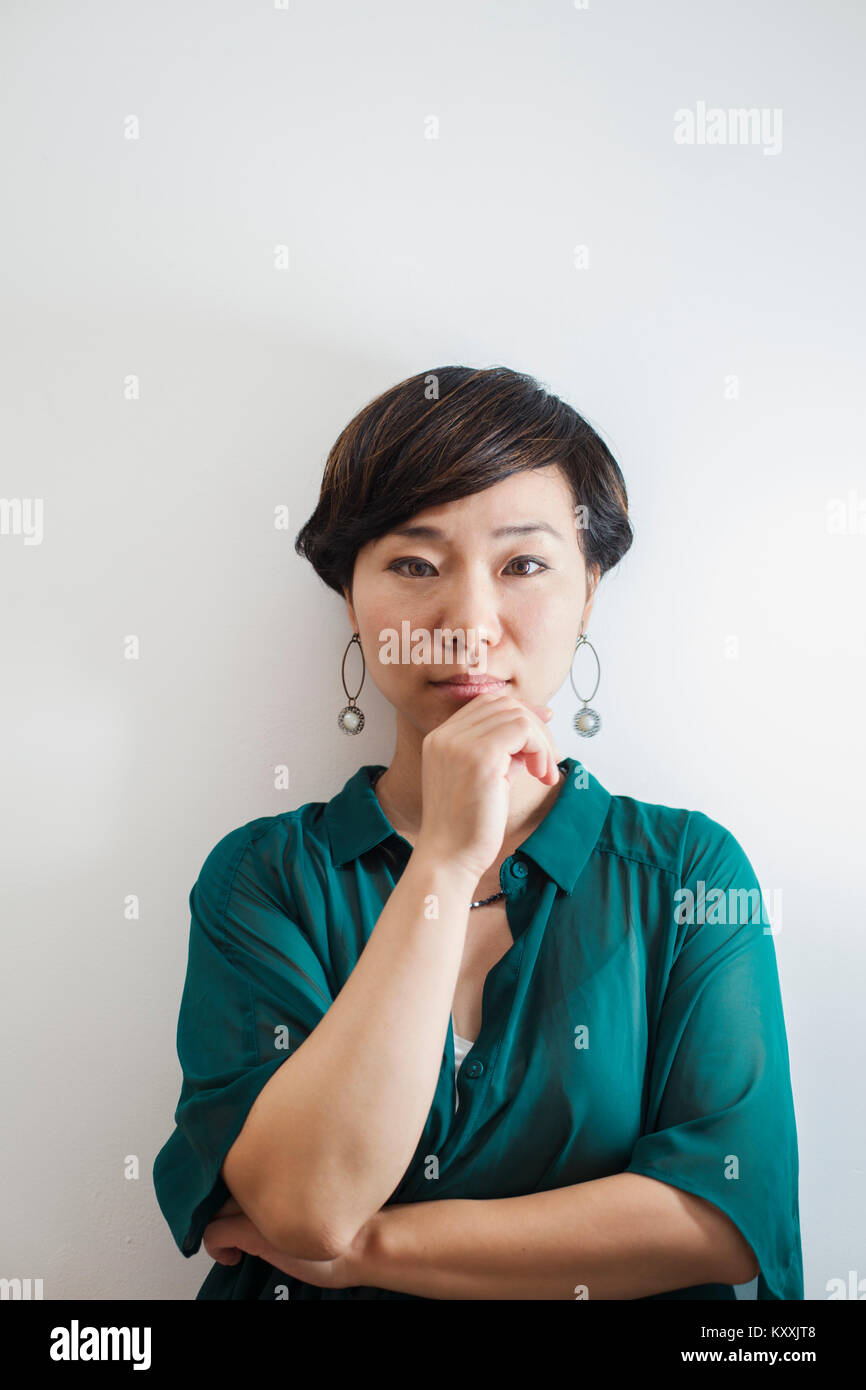 Frau mit kurzen schwarzen Haar grünes T-Shirt Standing in der Kunst Galerie, Hand am Kinn, an der Kamera schaut. Stockfoto