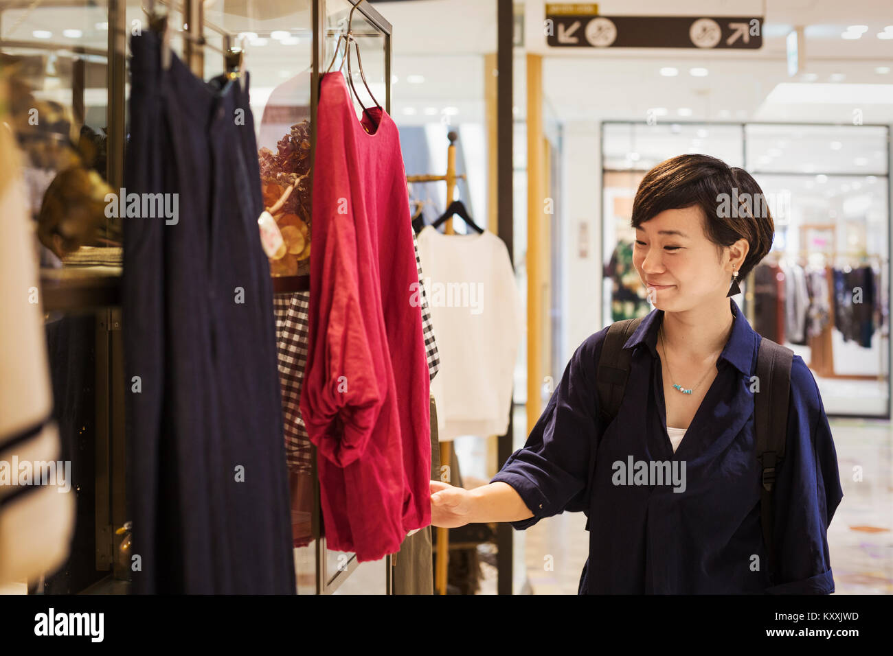 Frau mit schwarzen Haaren trägt blaue Hemd steht drinnen, an Kleidung in einem Geschäft suchen. Stockfoto