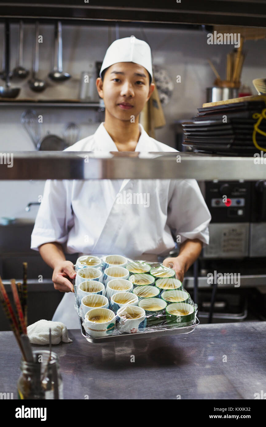 Koch arbeiten in der Küche eines japanischen Sushi Restaurant, holding Fach mit kleinen Schüsseln mit Essen. Stockfoto