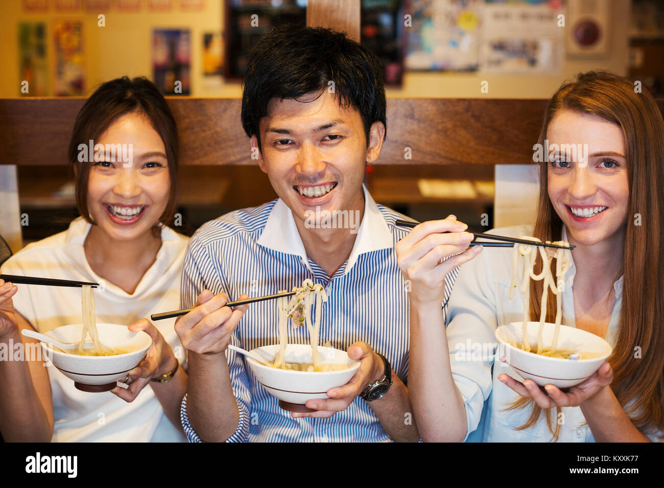 Drei lächelnde Menschen sitzen sidy nebeneinander an einem Tisch in einem Restaurant, Essen von Schalen mit Stäbchen. Stockfoto