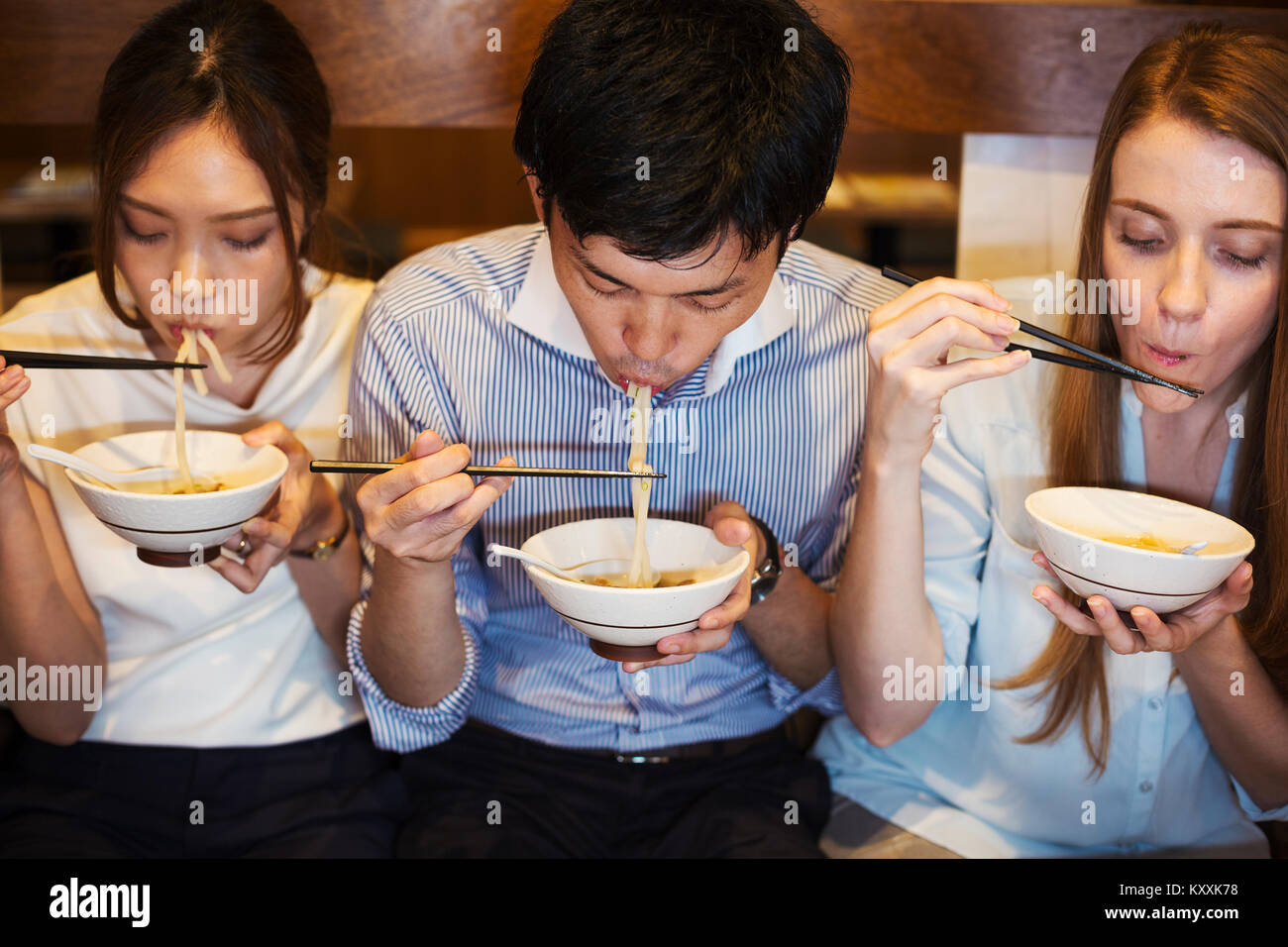 Hohe Betrachtungswinkel von drei Personen sitzen sidy nebeneinander an einem Tisch in einem Restaurant, Essen von Schalen mit Stäbchen. Stockfoto