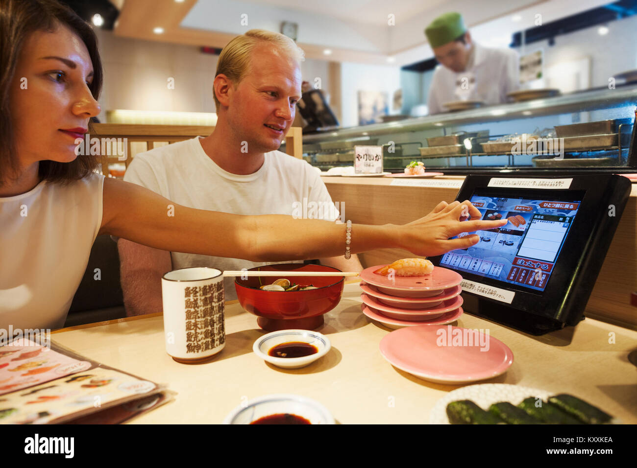 Junger Mann und eine Frau an einem Tisch in einem asiatischen Fast Food Restaurant sitzen, essen, Sushi, auf der Suche nach Touchscreen auf Ihrem Tisch. Stockfoto
